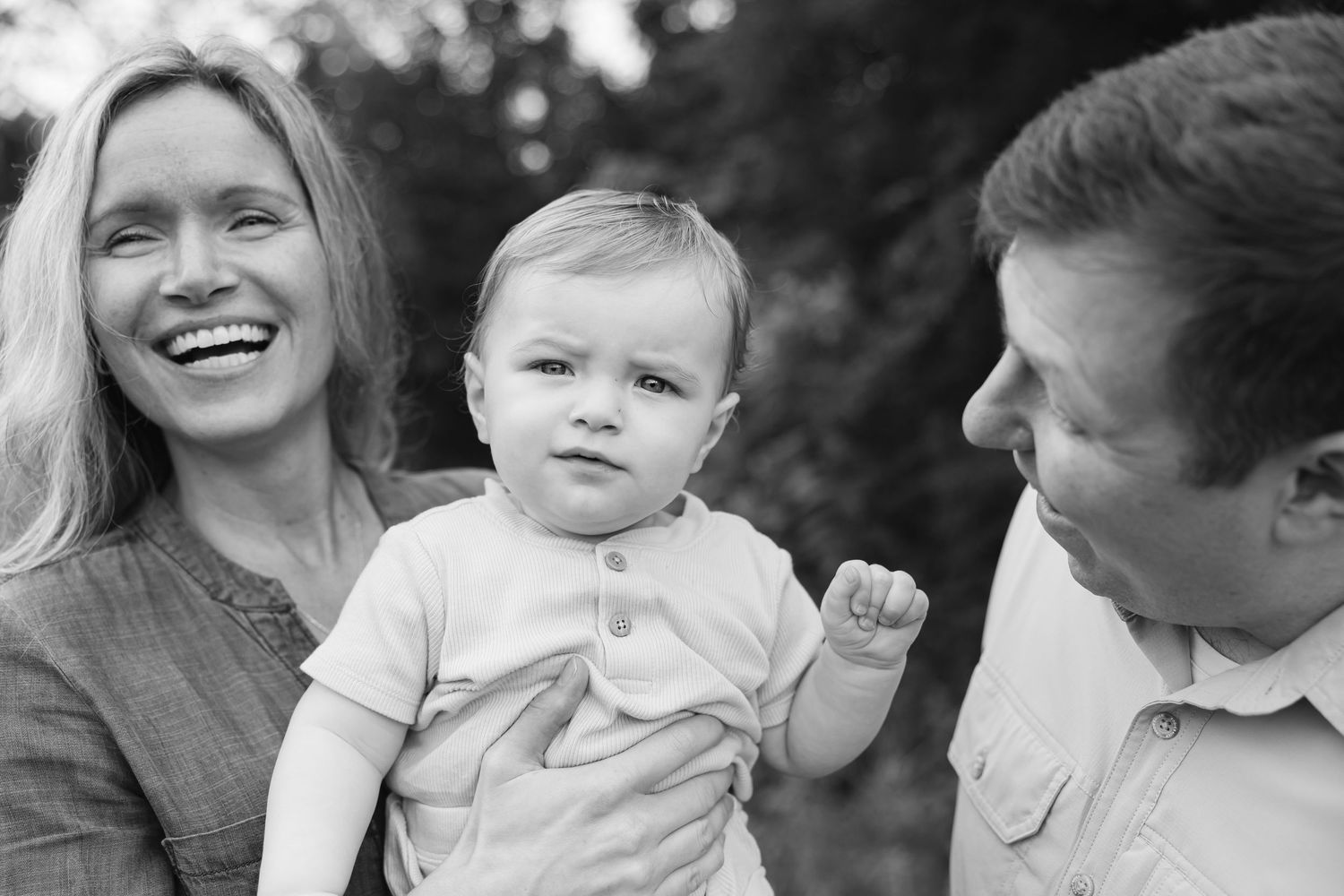 Smiling parents holding their baby during a candid family photography session in Tipp City, Ohio.