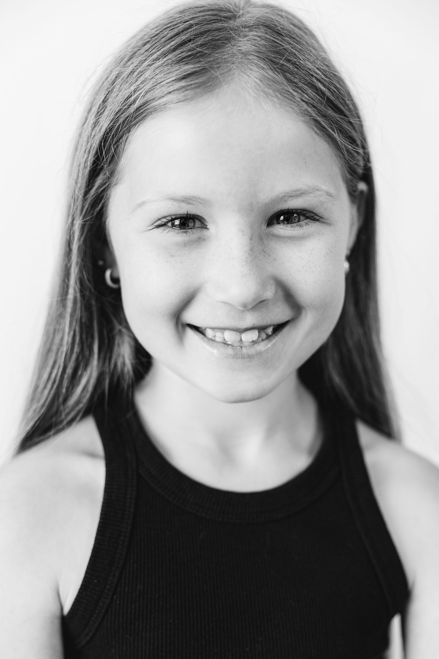 Black and white portrait of a smiling young girl with long hair wearing a black tank top.