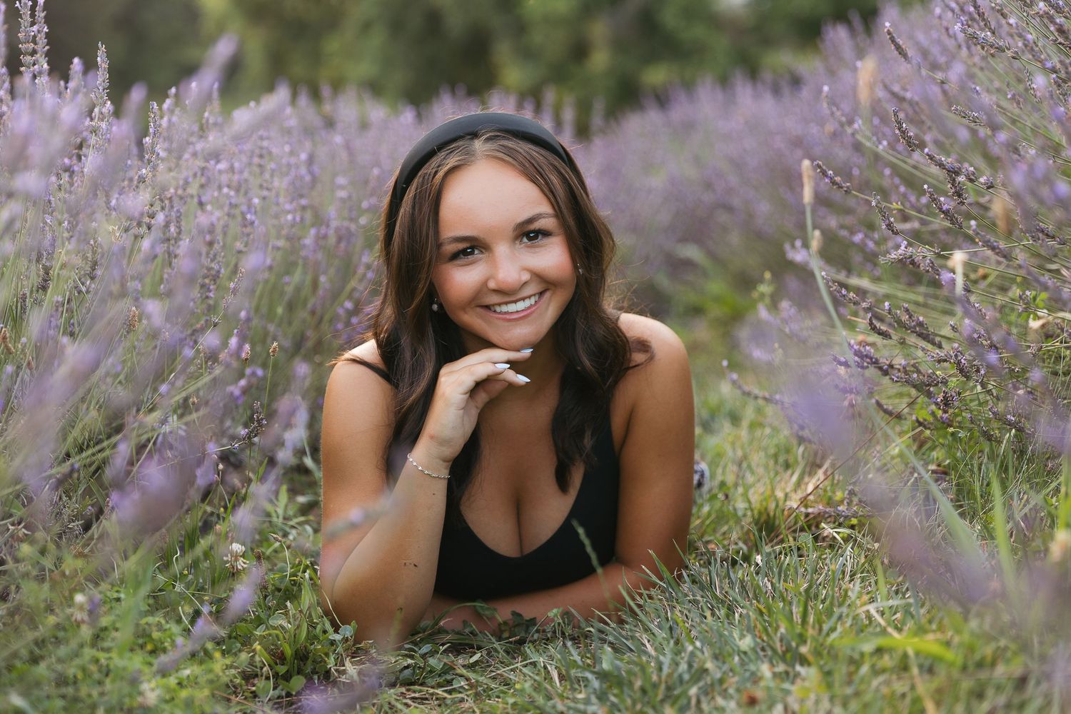Smiling young woman lying in a lavender field, wearing a black top, surrounded by purple blooms. Katie Chamberlain Photography