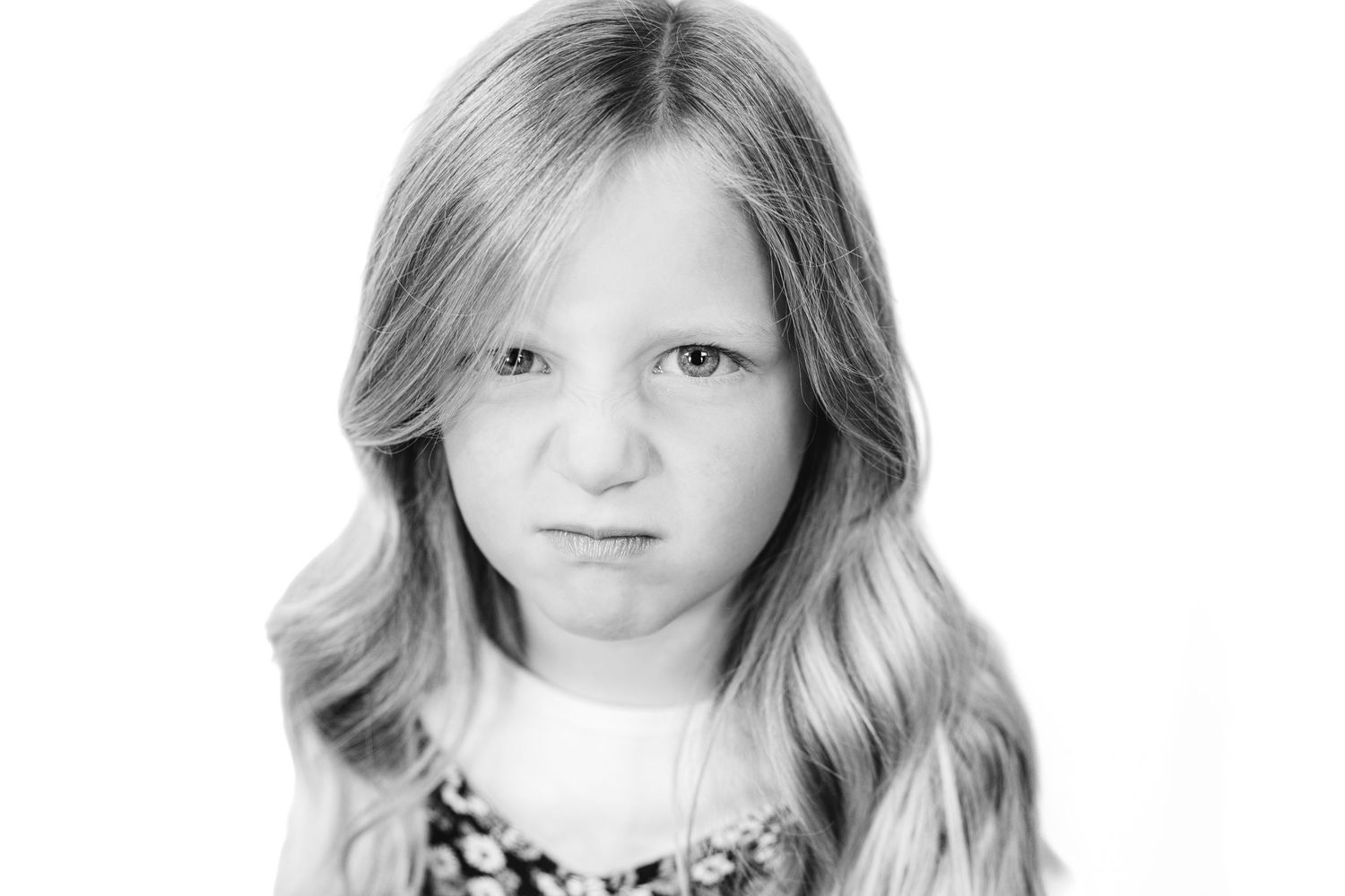 Black and white portrait of a young girl with long blonde hair making an angry, pouty facial expression.