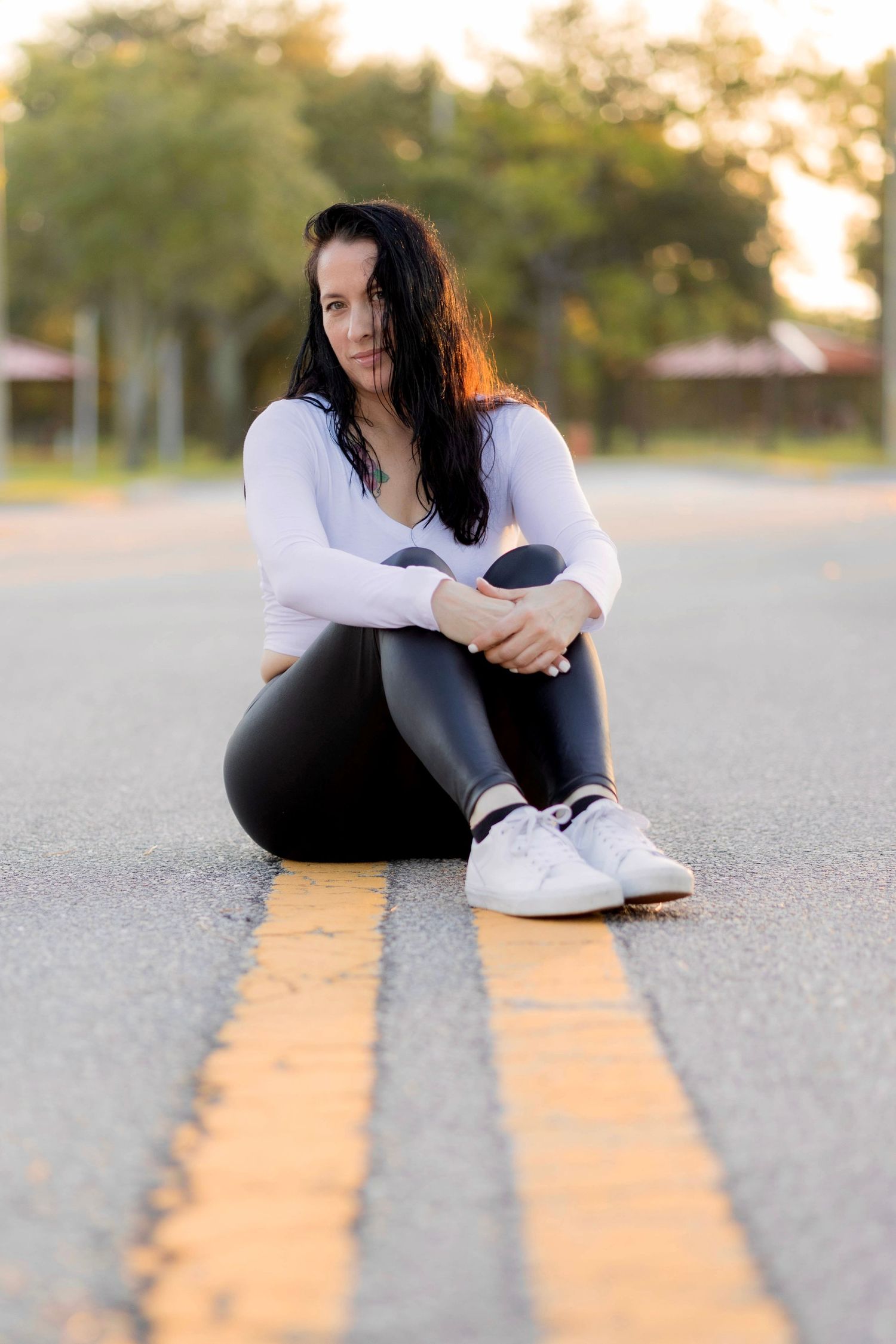Woman in white sweater sitting on yellow road lines during golden hour photoshoot.