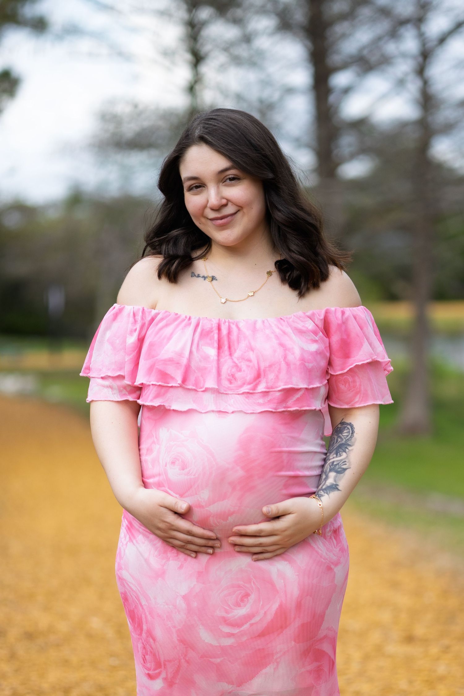 Woman in pink off-shoulder dress poses in outdoor setting with natural lighting.