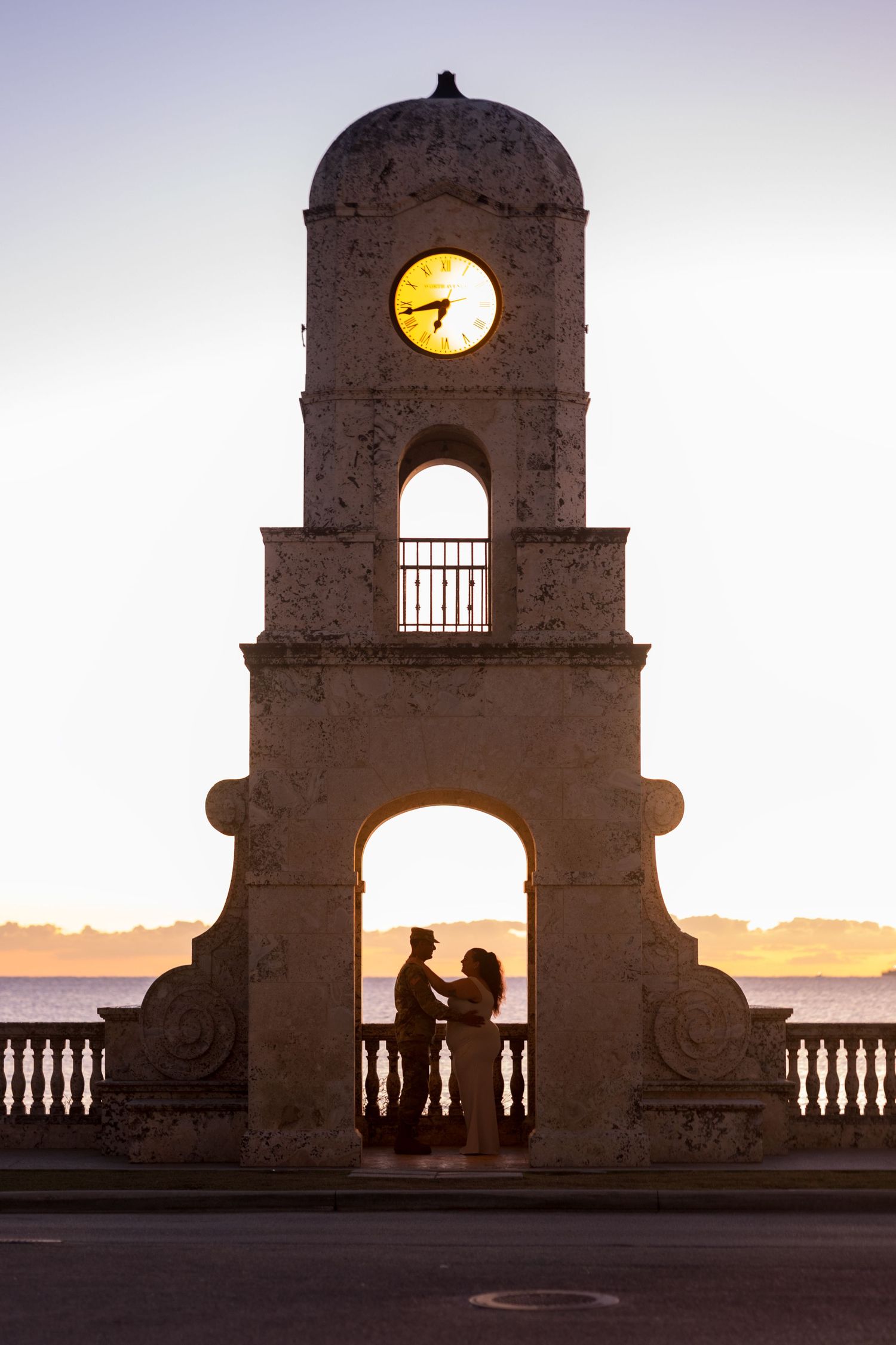 Silhouettes against sunset through historic stone archway at Palm Beach Worth Avenue.