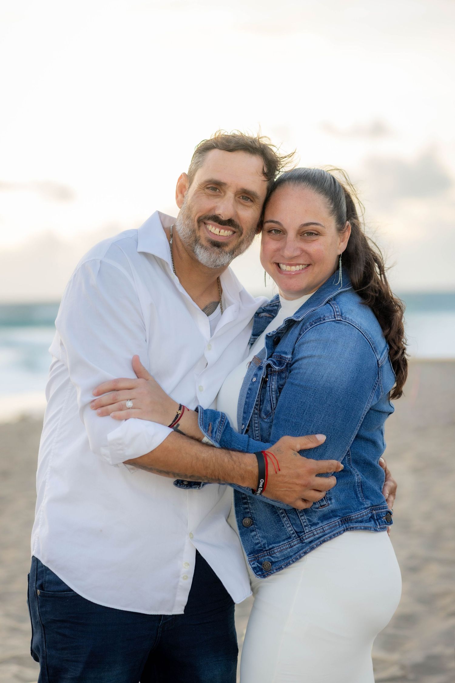 Casual beach engagement photos with denim jacket and white shirt at sunset.