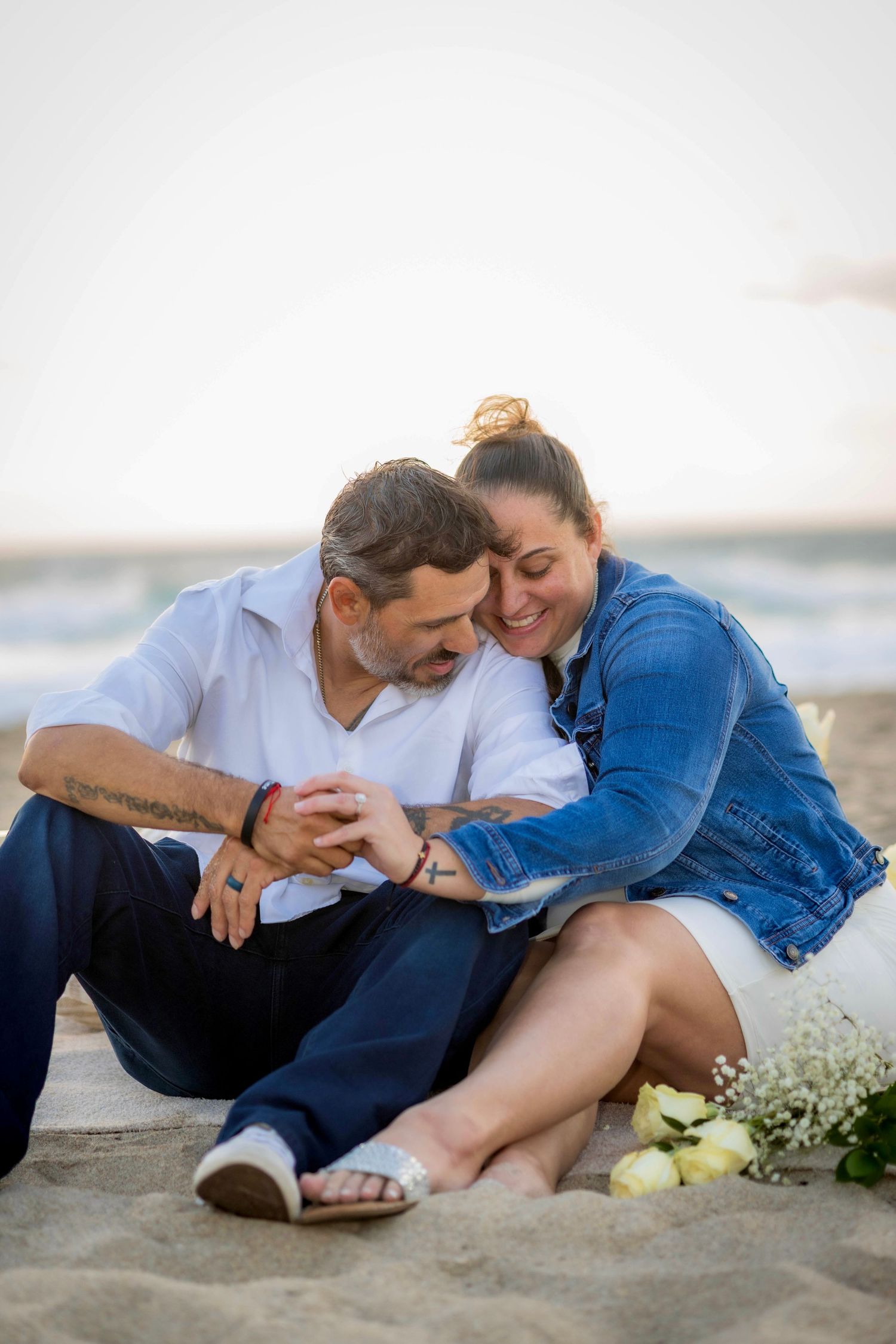 Couple sharing intimate moment while sitting together on sandy beach at sunset.