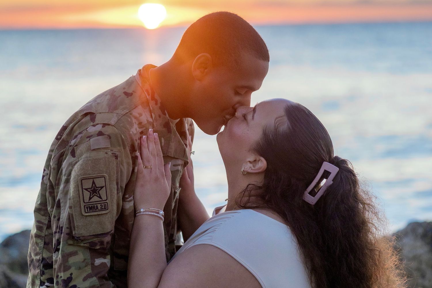 Silhouetted couple sharing intimate moment during sunset beach photoshoot.