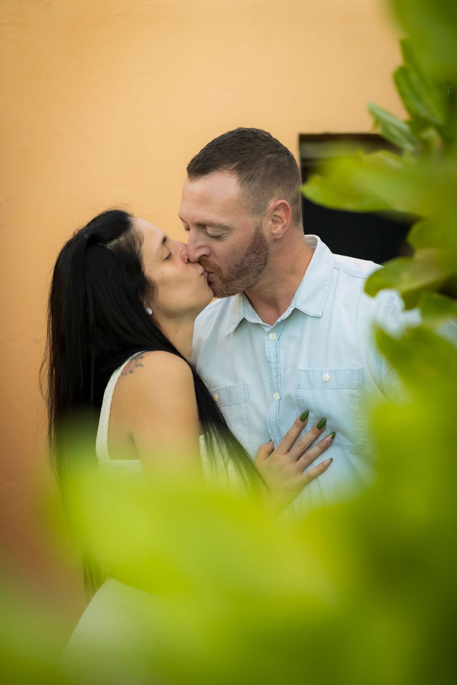 Romantic couple sharing intimate moments through green foliage in warm lighting.