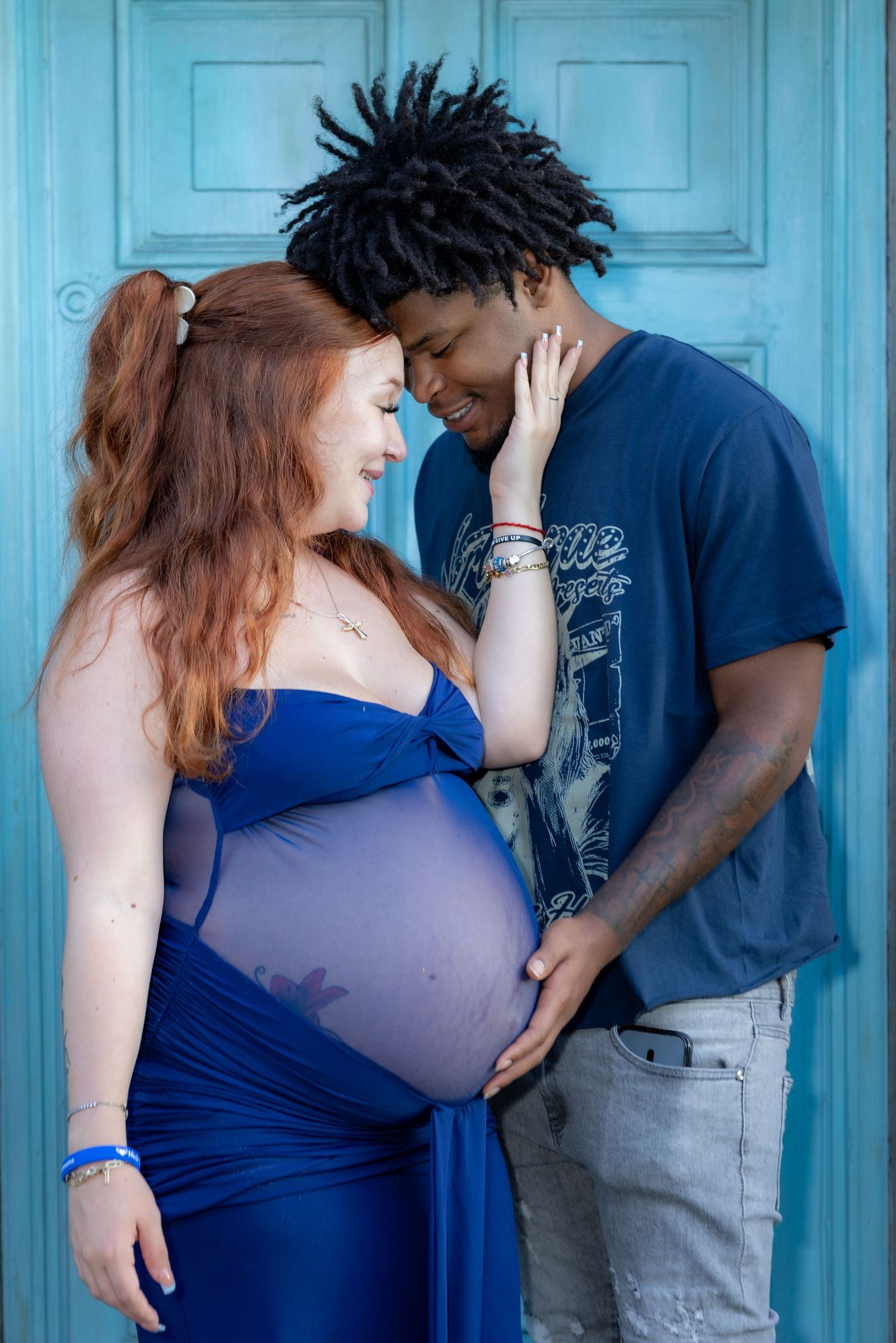 Interracial couple sharing a tender moment during a maternity photoshoot in front of a blue door.