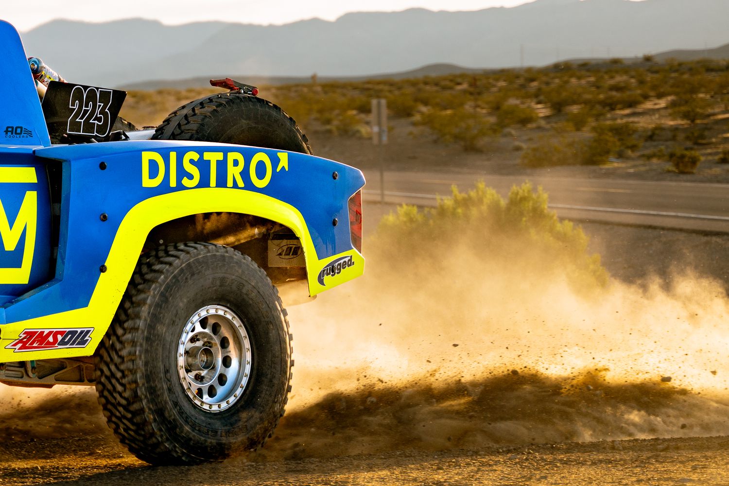 Ingram Distro trophy truck kicking up dust while racing through desert terrain on a dirt track.