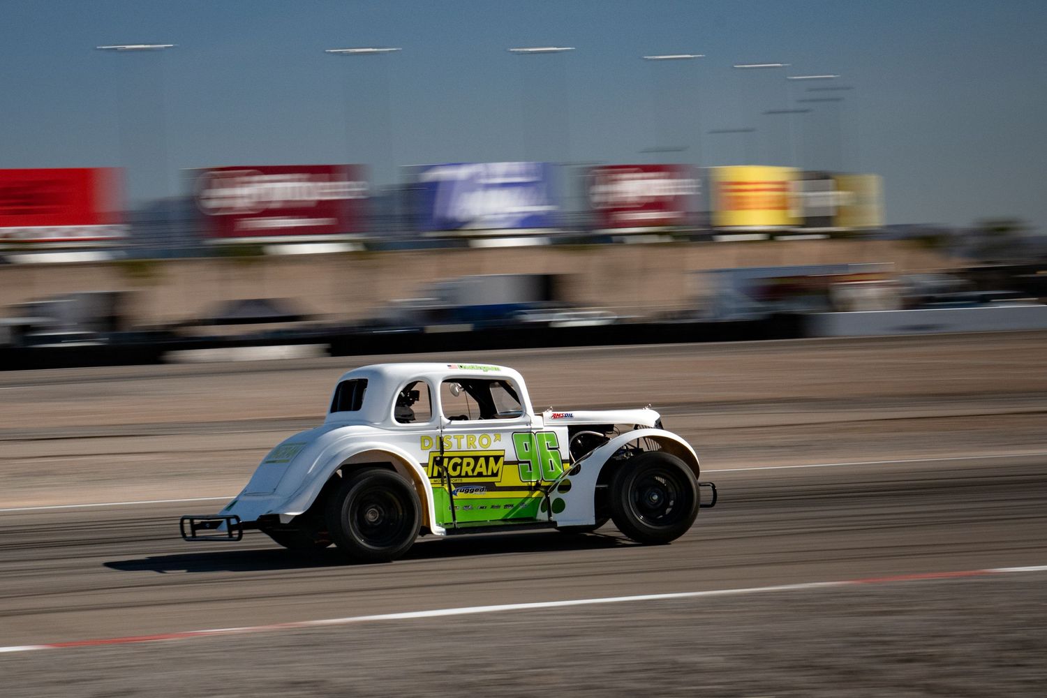 A white and green vintage-style legend race car speeding on a racing track during a sunny day competition.