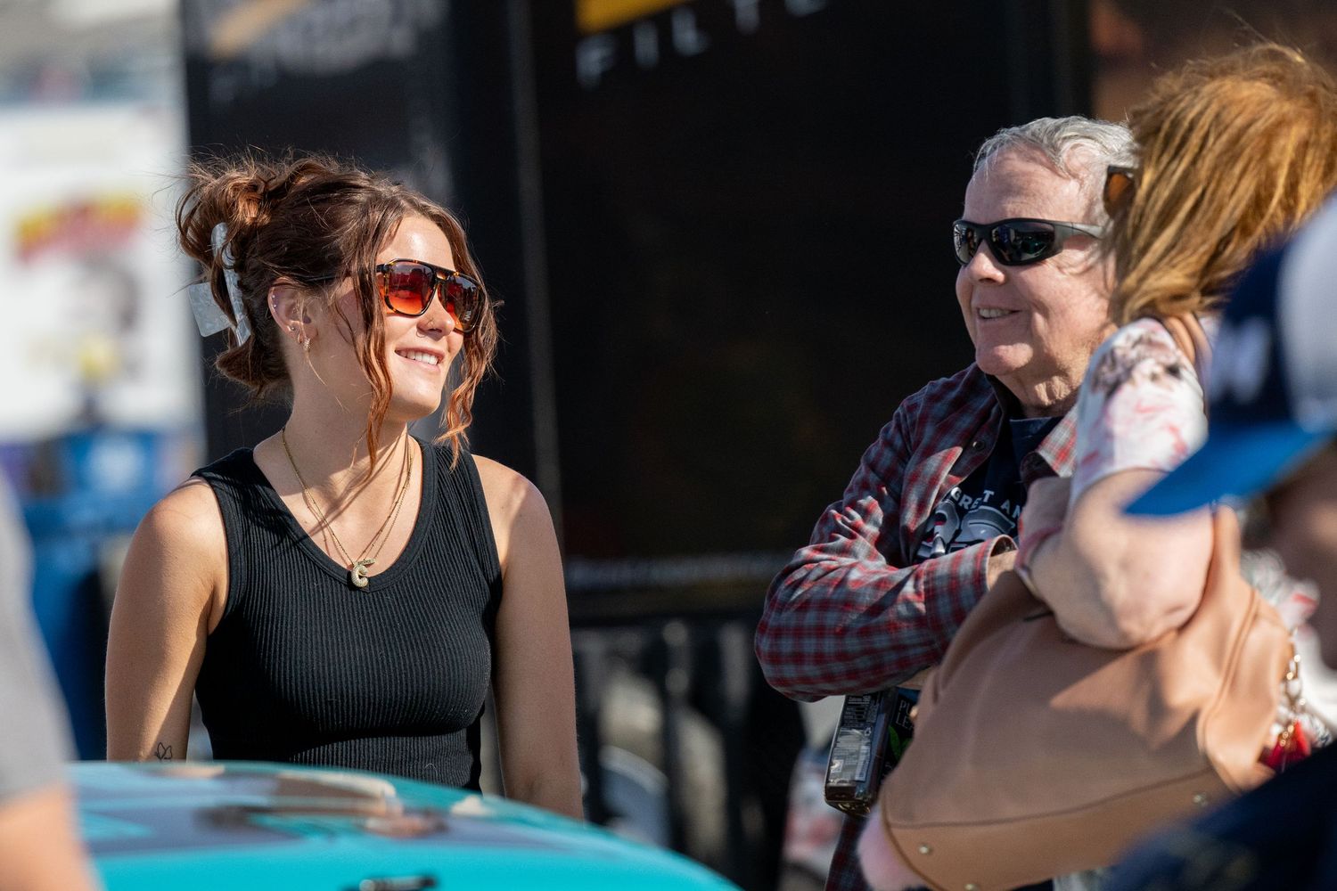 Woman in black top laughing with older man in plaid shirt at outdoor NASCAR racing event.