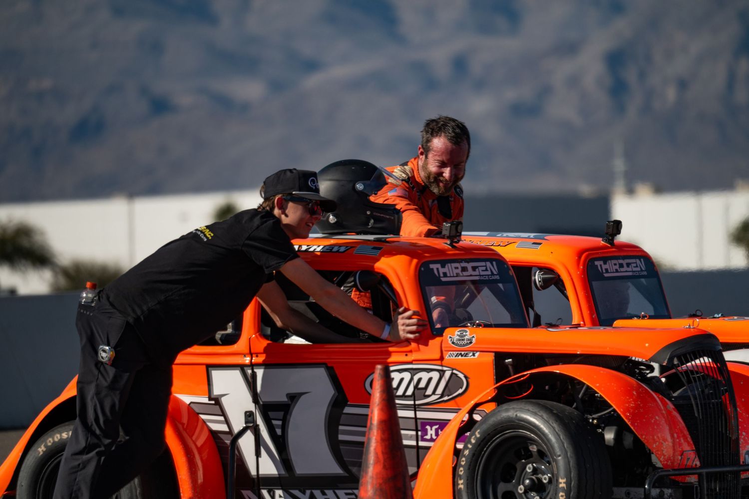 Racing crew members assisting driver in orange number 17 legend car at pit area.