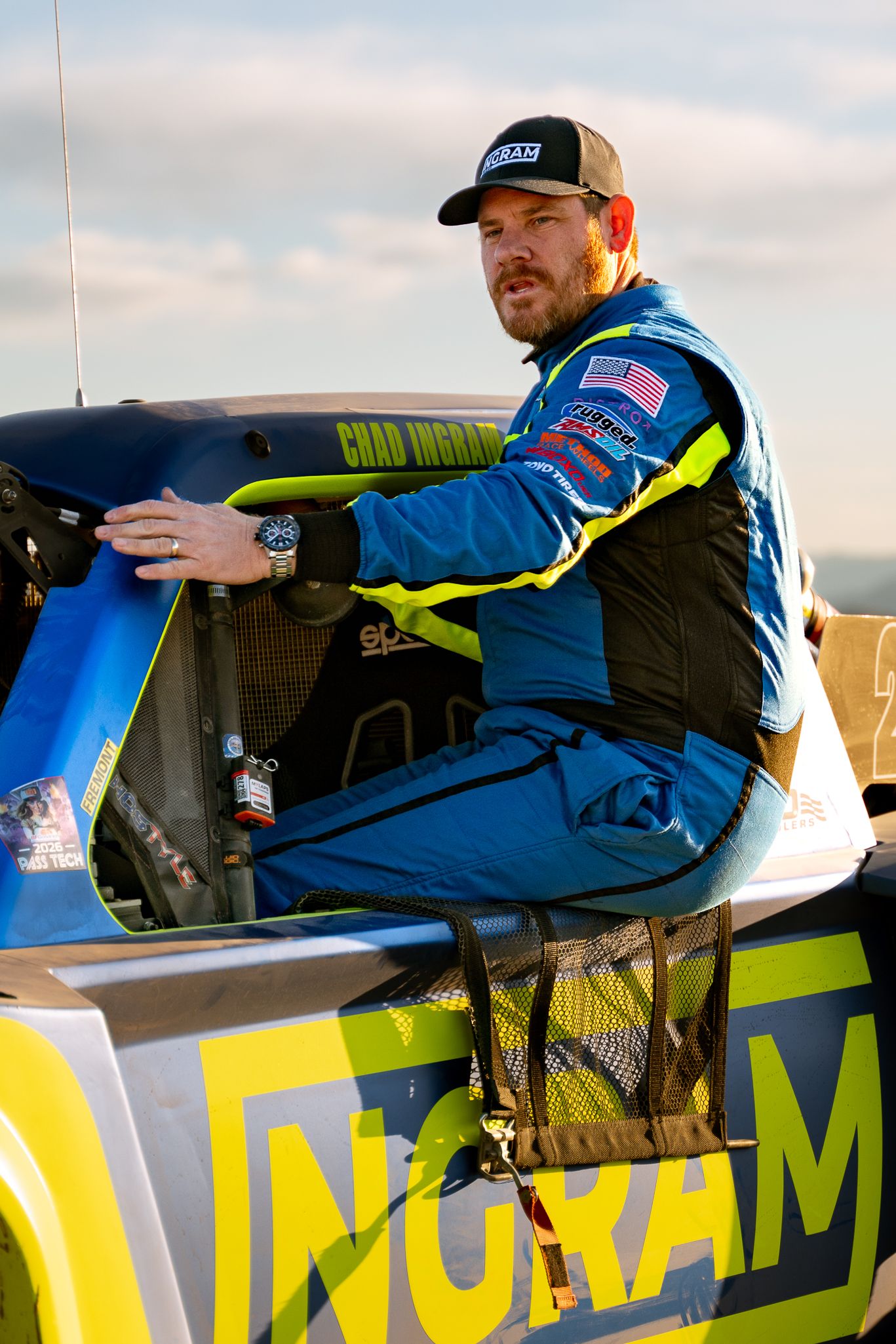 Chad Ingram in blue and yellow racing suit sitting on edge of Ingram off-road trophy truck cockpit.