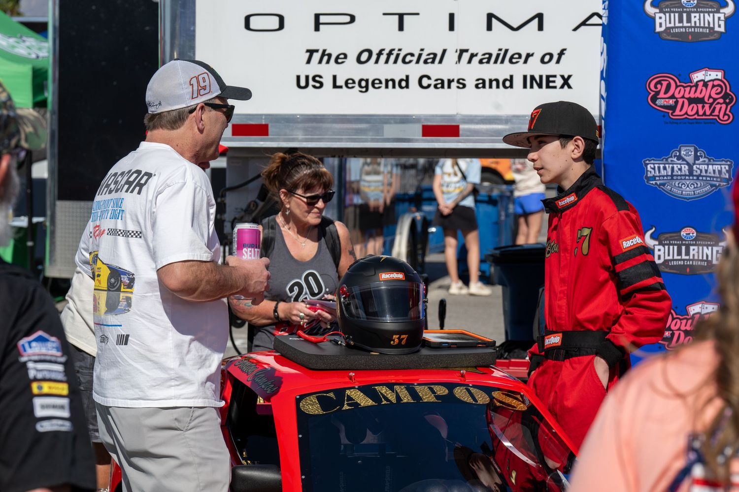 Young race driver in red suit with helmet at NASCAR vendor booth talks to community at NASCAR
