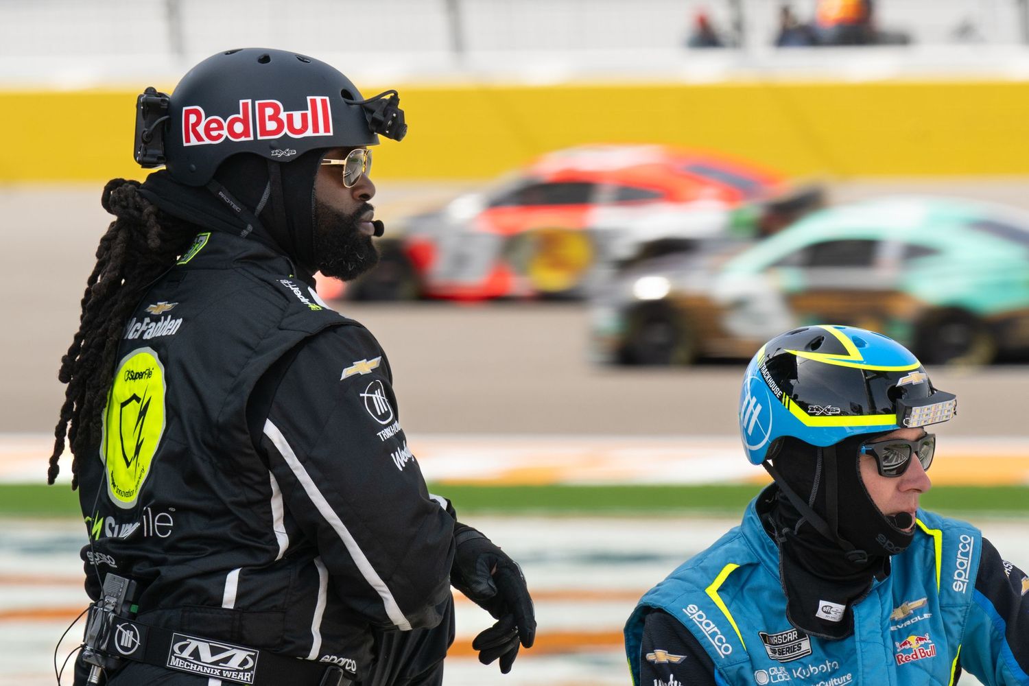 Two Red Bull NASCAR pit crew members watching race action on track at Las Vegas Speedway.