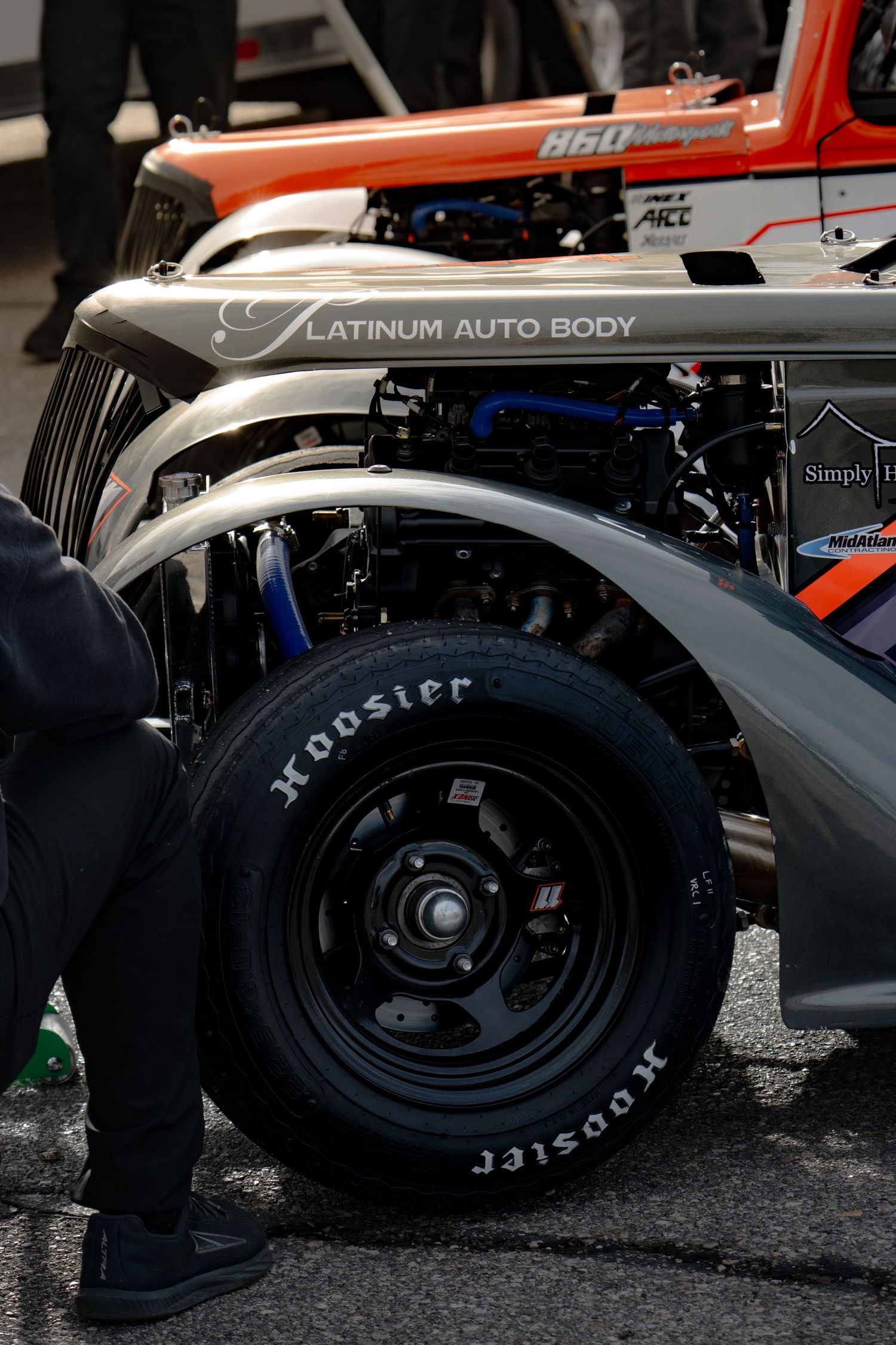 Close-up of Hoosier racing tires on a silver Platinum Auto Body sponsored race car in pit lane.
