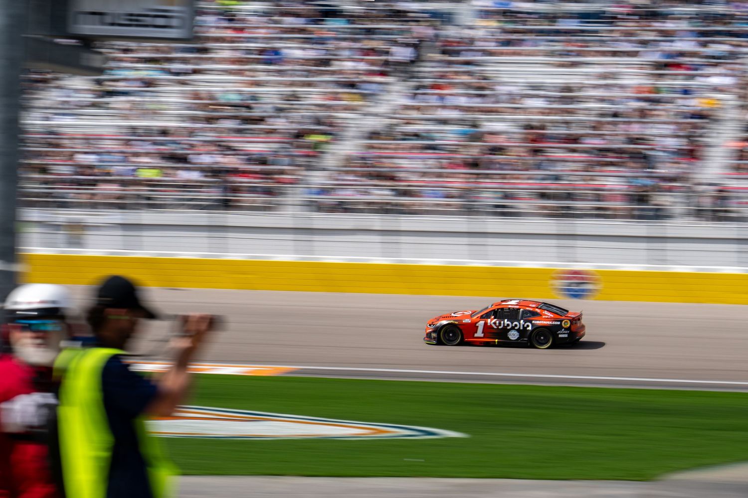 NASCAR race car speeding past packed grandstands at Las Vegas Motor Speedway during race.