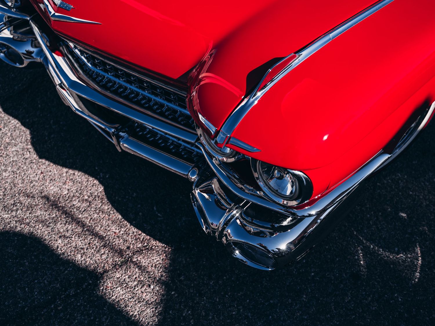 Close-up of a classic red vintage car showcasing its chrome bumper and iconic tail fin design.