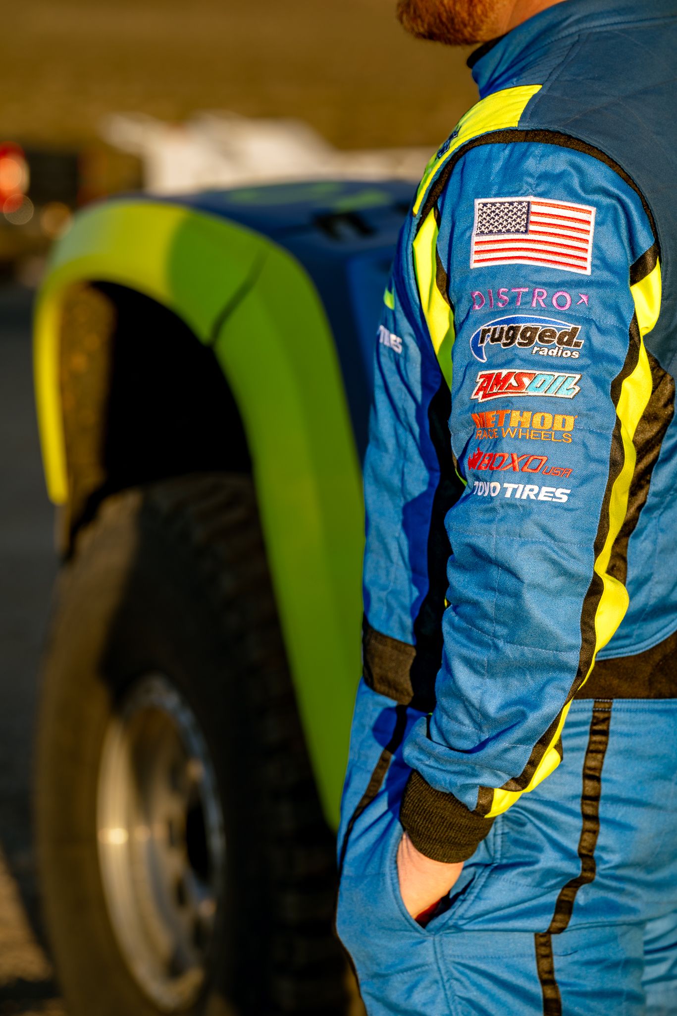 Close-up of blue and yellow racing suit sleeve with sponsor logos including Distro, Rugged Radios, and Toyo Tires.
