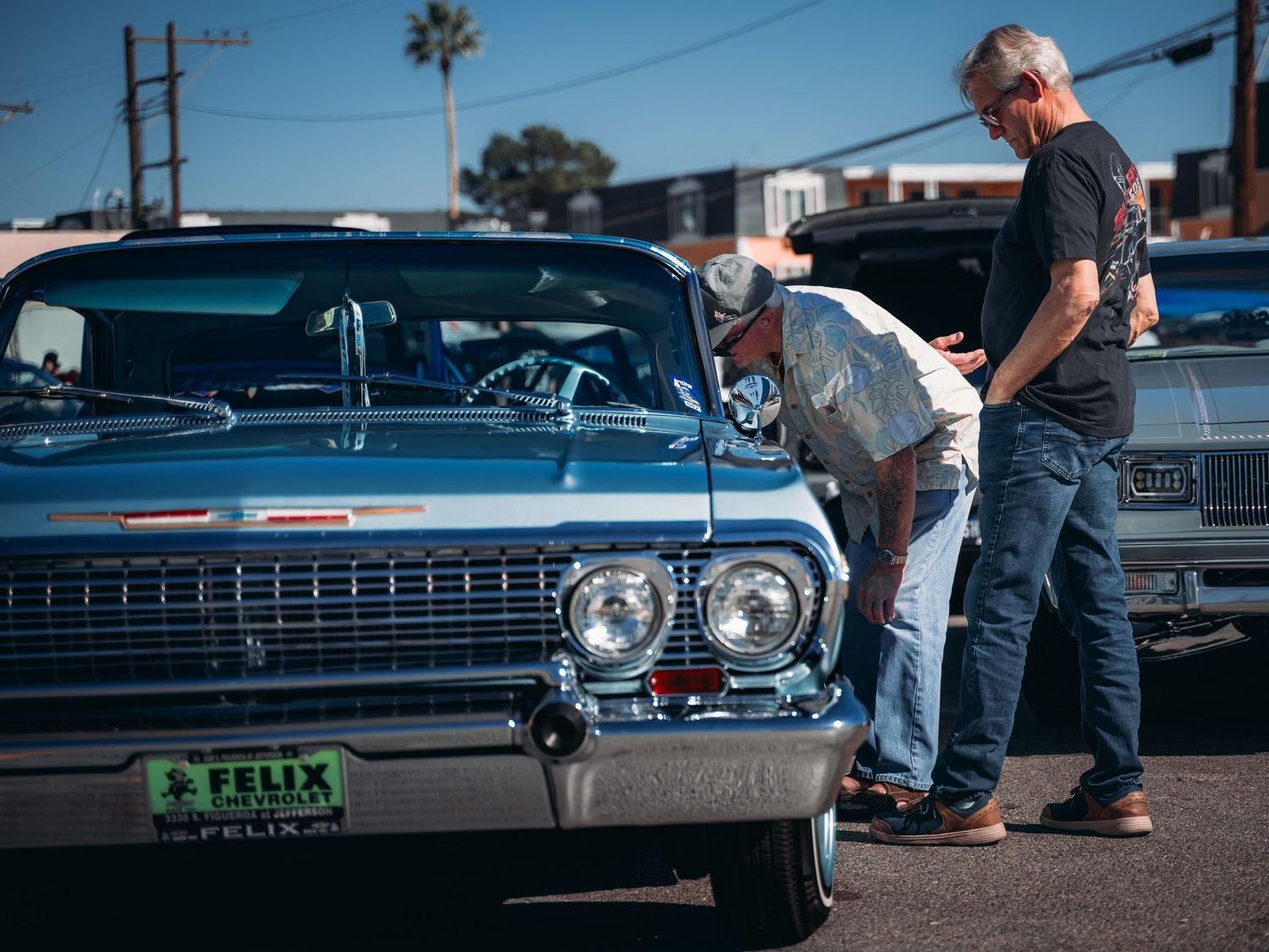 Two men inspecting a classic blue 1964 Chevrolet Impala lowrider at Super Saturday Weekend at The STRAT in Las Vegas