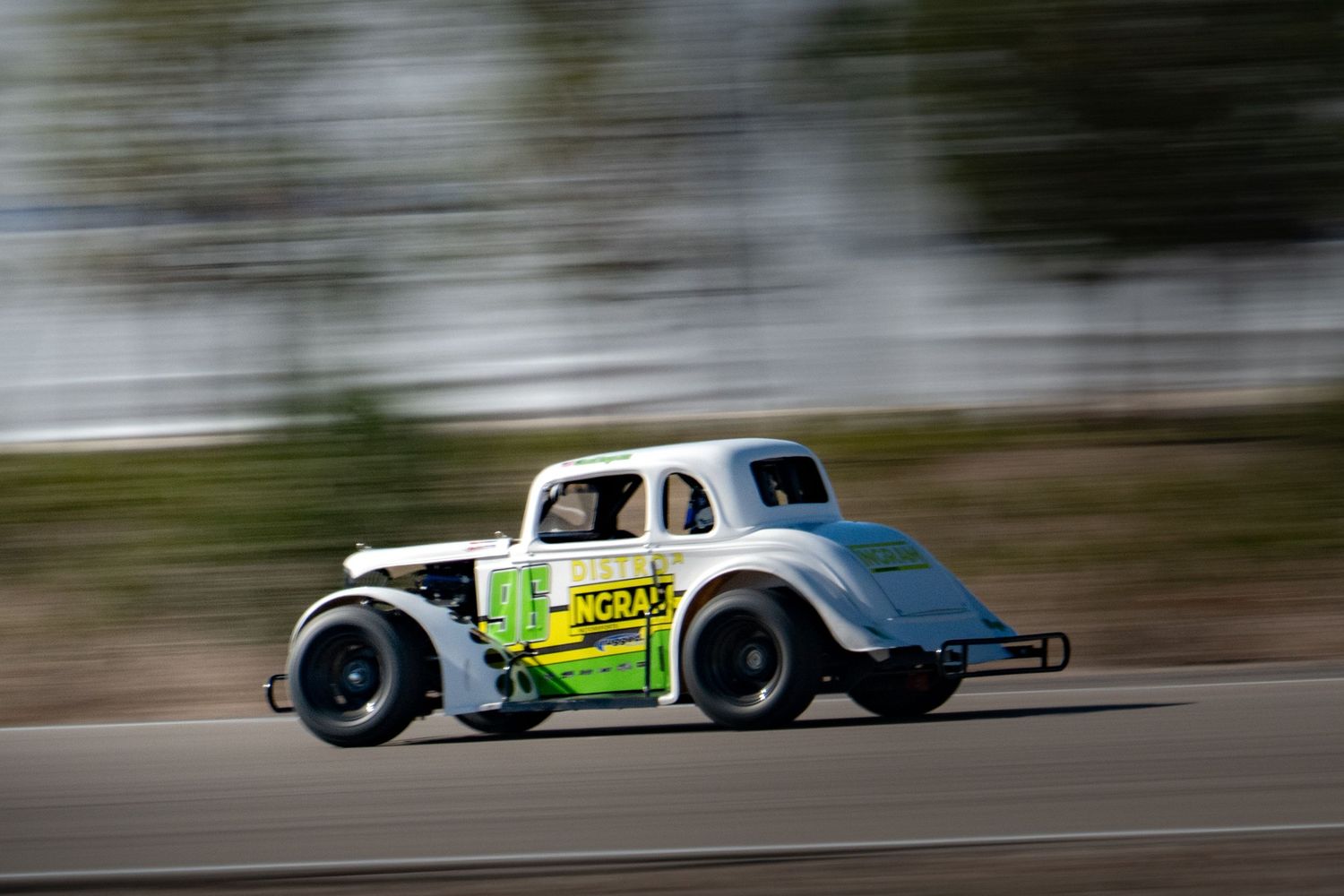 Green and white vintage legend race car speeding along a racing circuit track.
