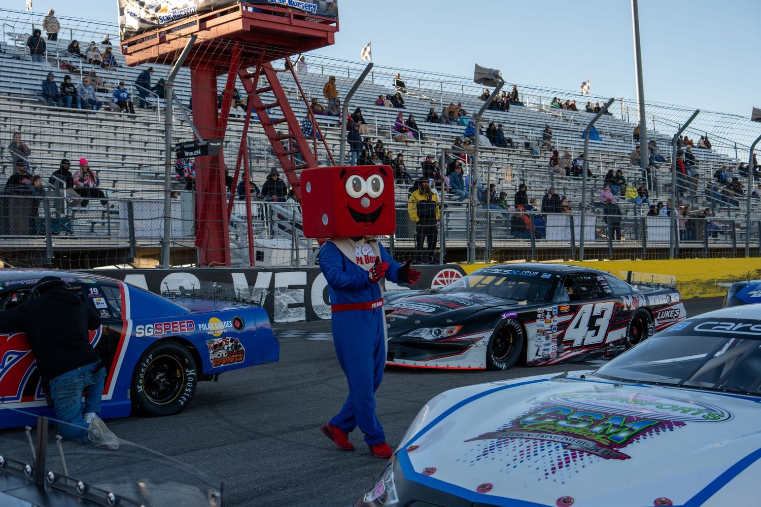 Racing mascot  Pit boss poses between stock cars on pit lane at NASCAR event.