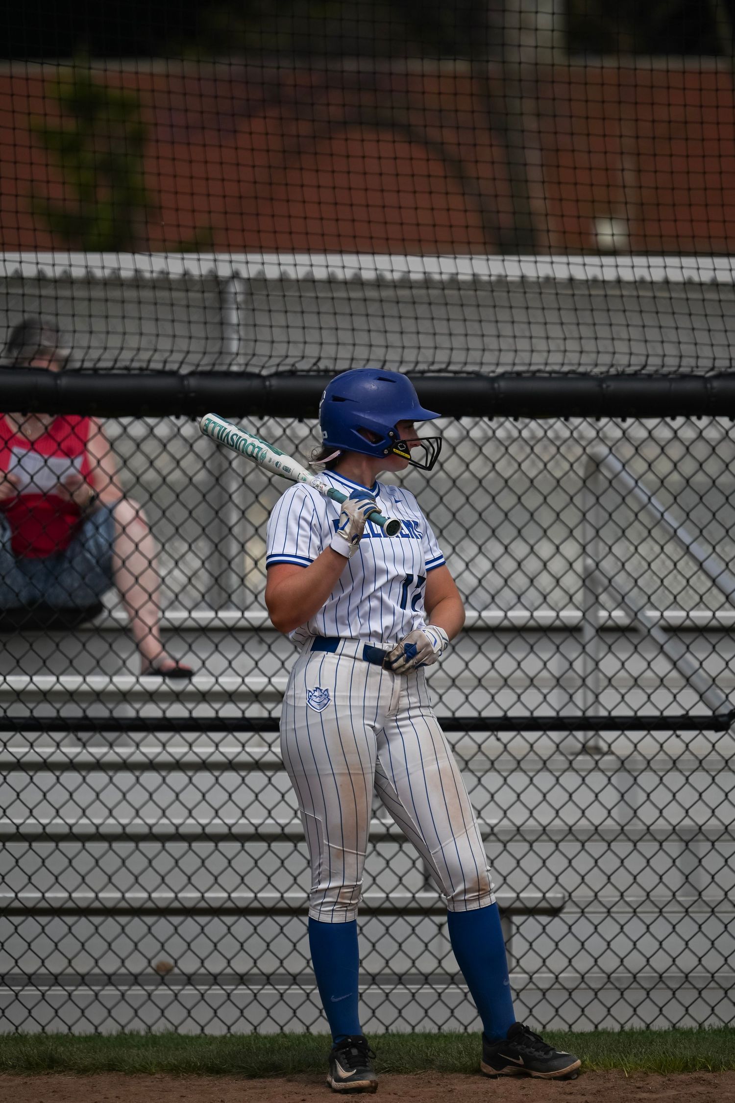 Female softball player in blue helmet and uniform stands ready to bat during a game.