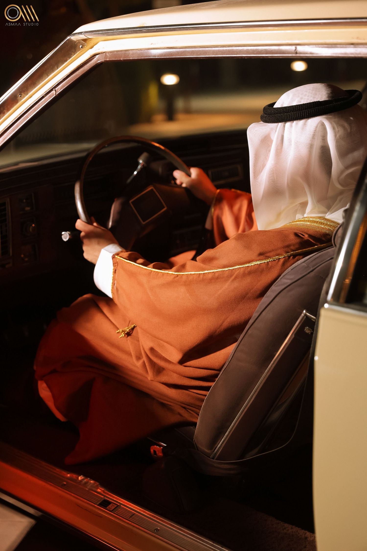 Person in traditional Middle Eastern dress sitting in luxury car interior at night.