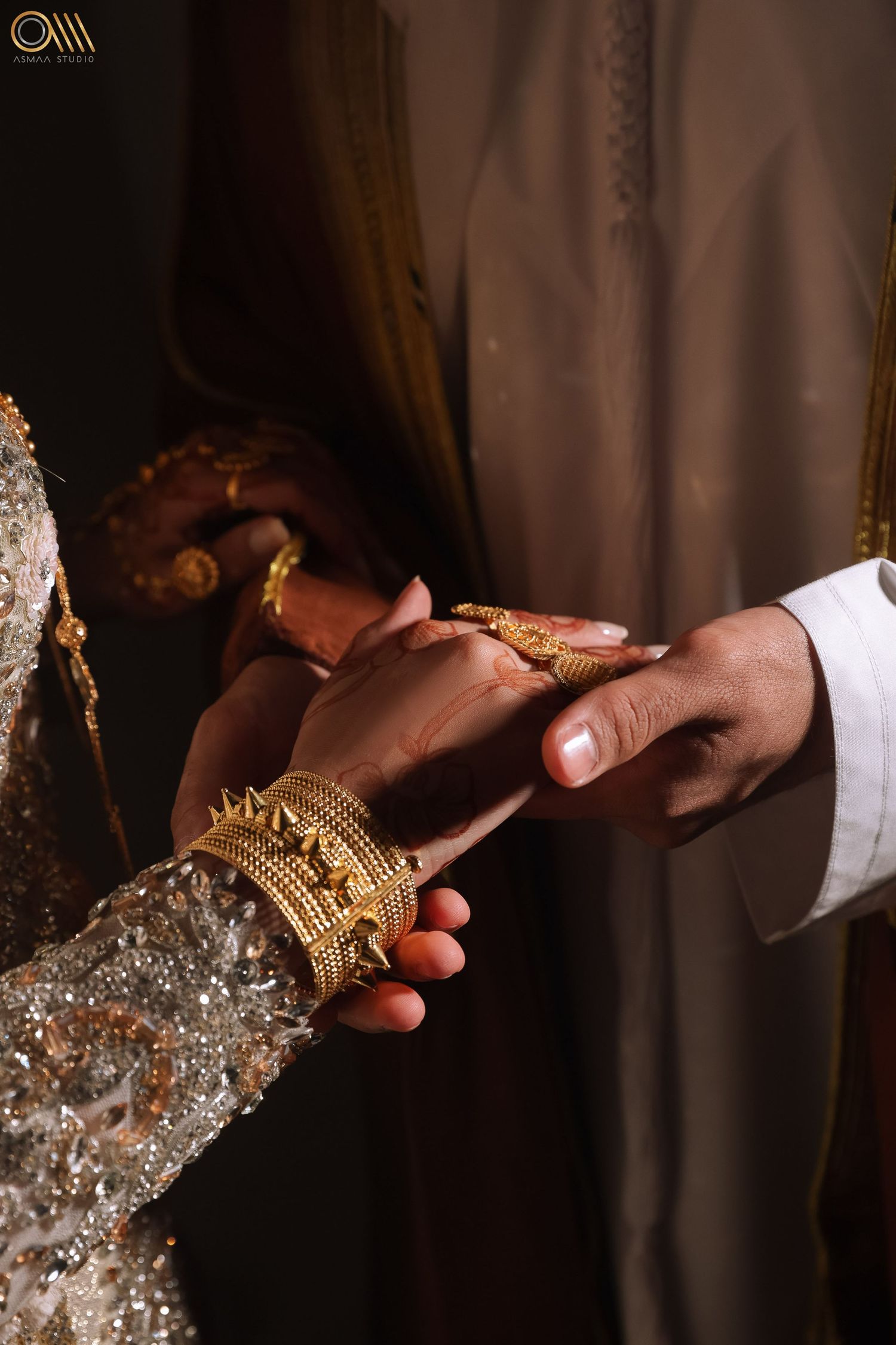 Close-up of hands wearing elegant bridal jewelry and accessories against a dark background.
