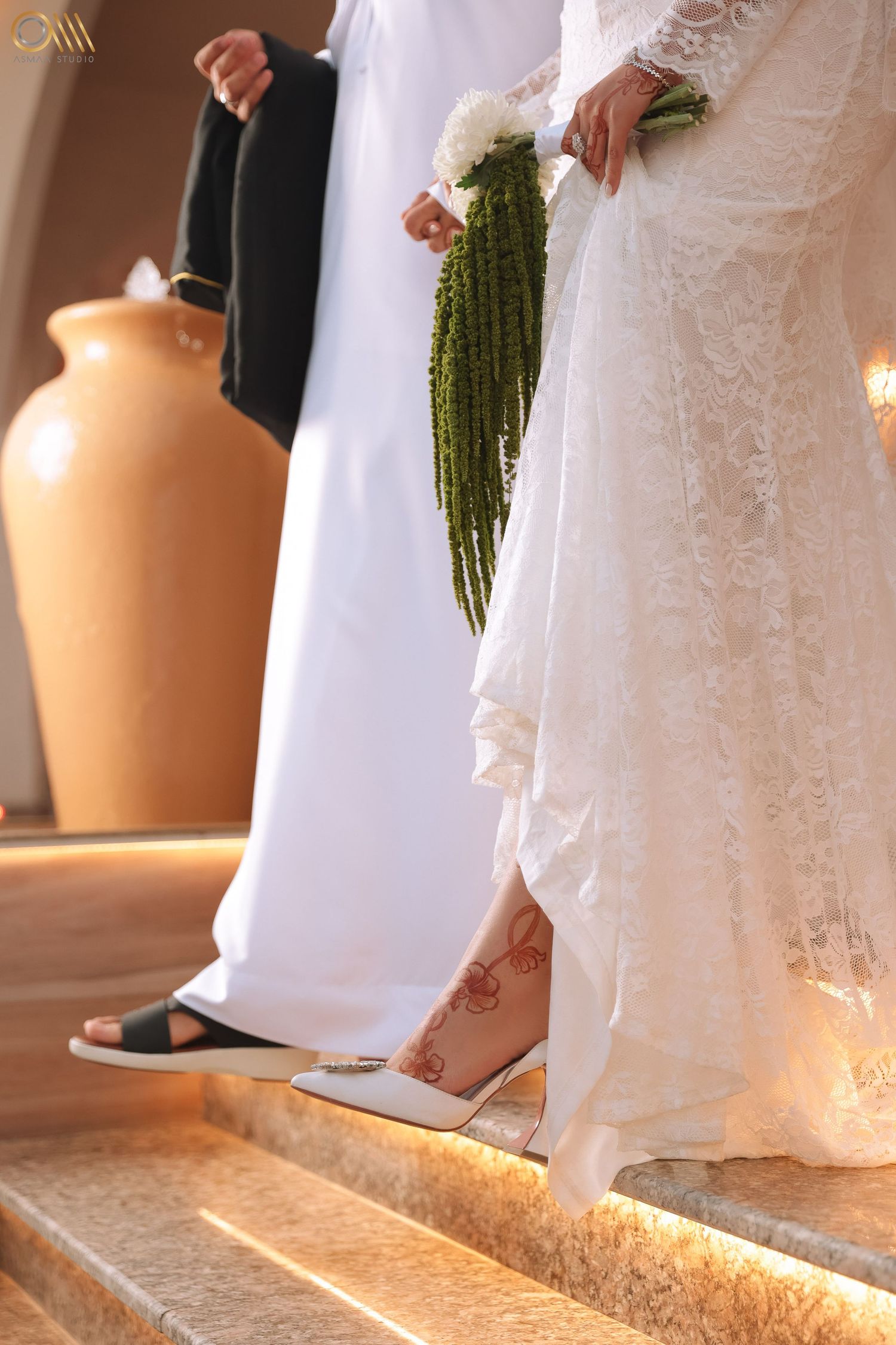 Detail shot of wedding dress hem and bouquet against warm backlit floor.