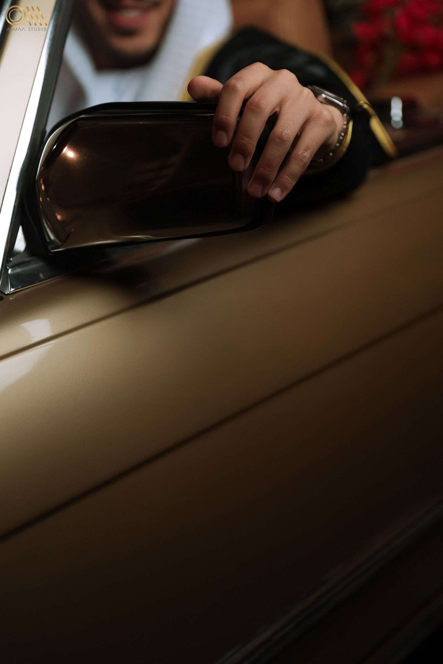 Hand adjusting side mirror of classic car with tan exterior.