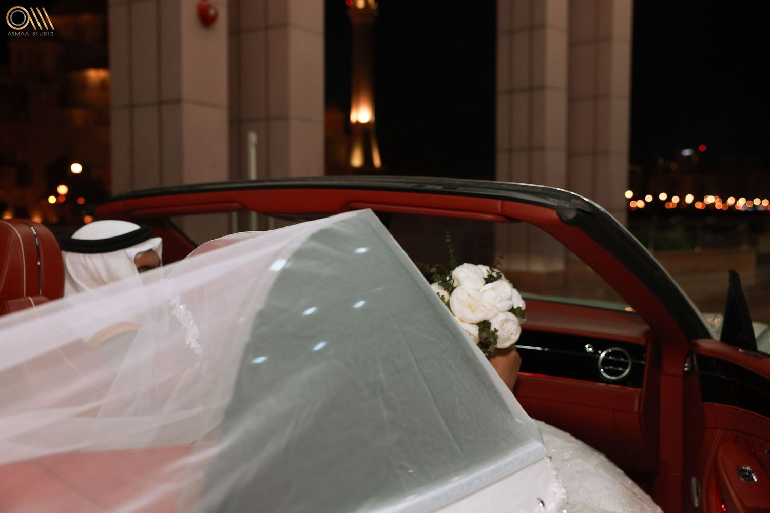 Luxury car decorated with white wedding ribbons and floral arrangements.
