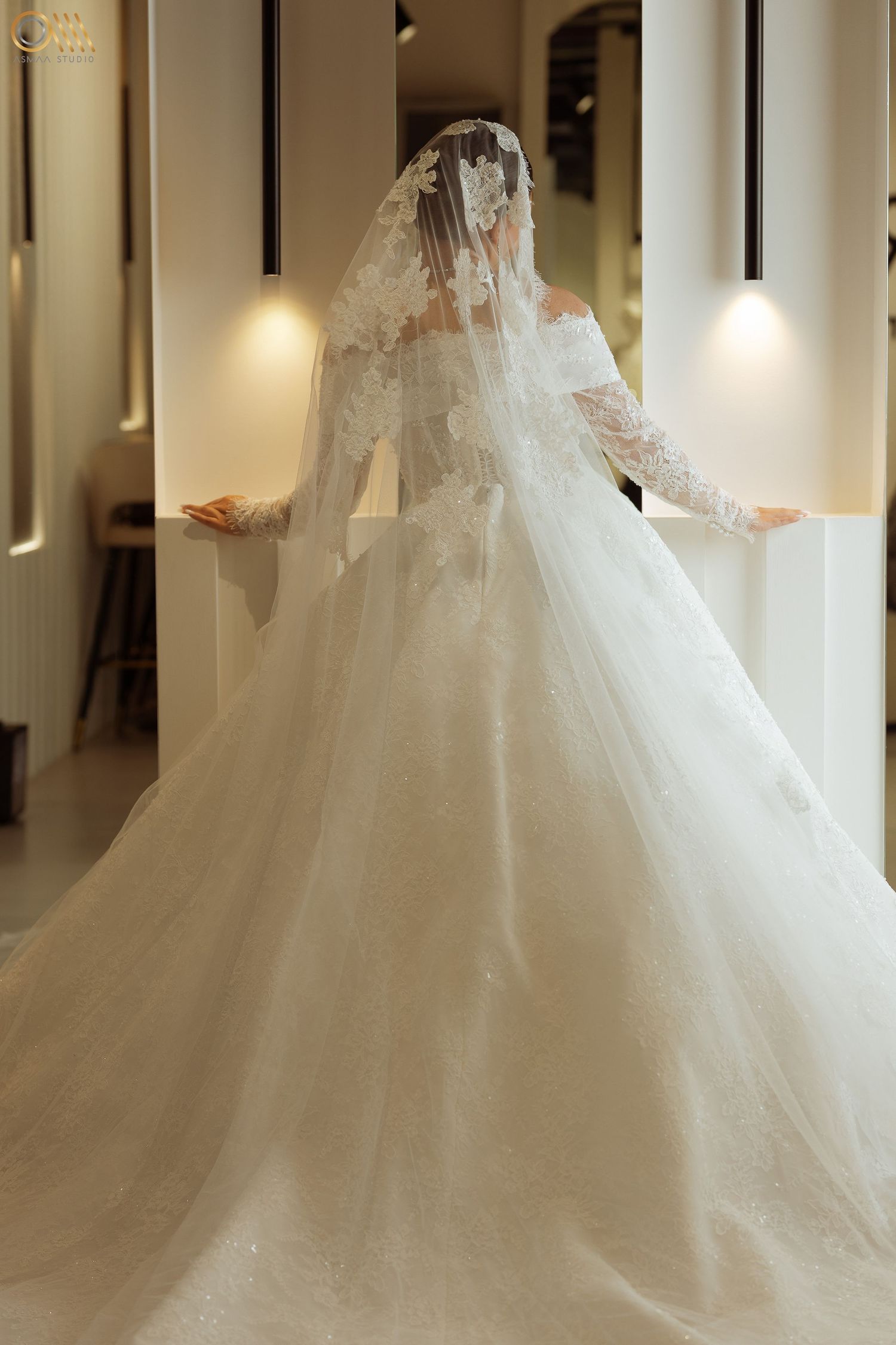Elegant white wedding gown with flowing train and veil captured in a brightly lit hallway.