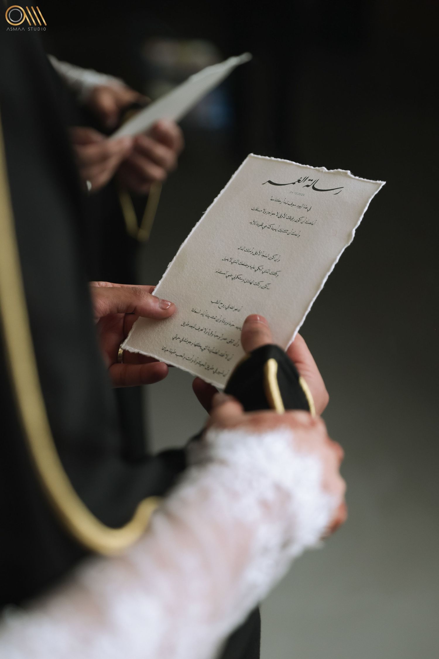 Wedding invitation card written in Arabic script held by hands in formal attire.