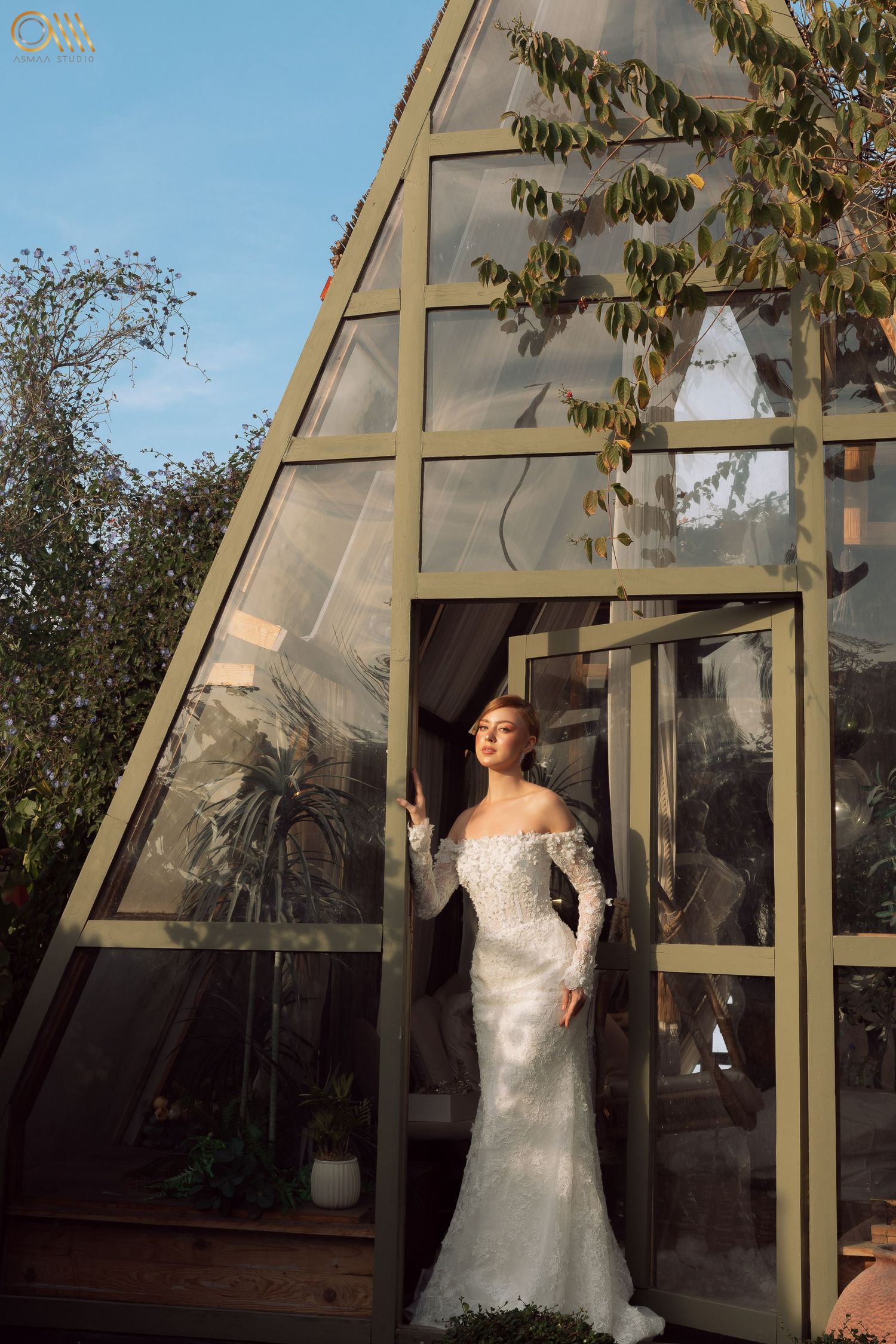 Dramatic bridal portrait taken in a sunlit greenhouse setting with glass walls.