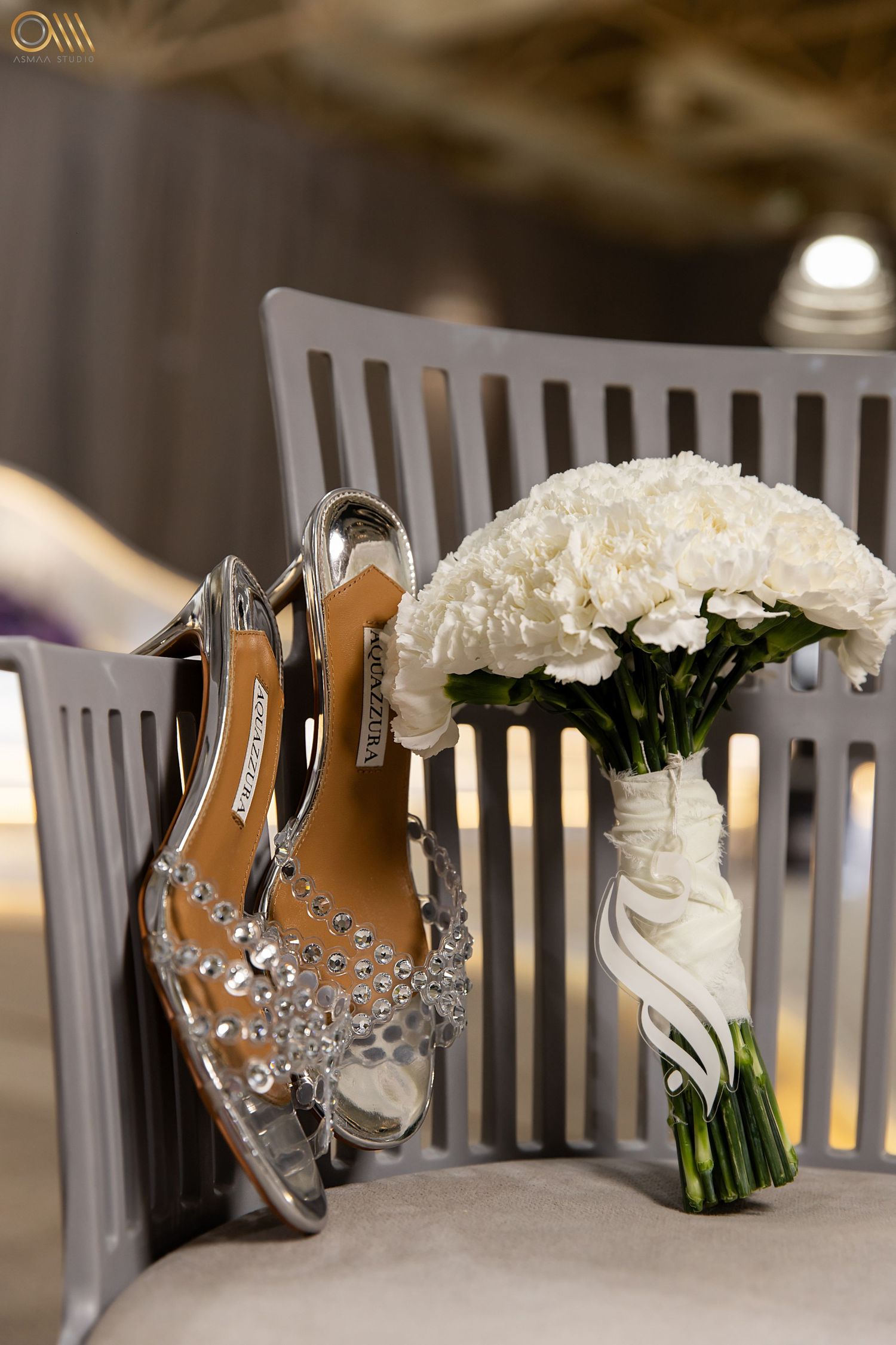 White bridal bouquet and elegant silver jewelry displayed on wooden chairs for wedding preparation.