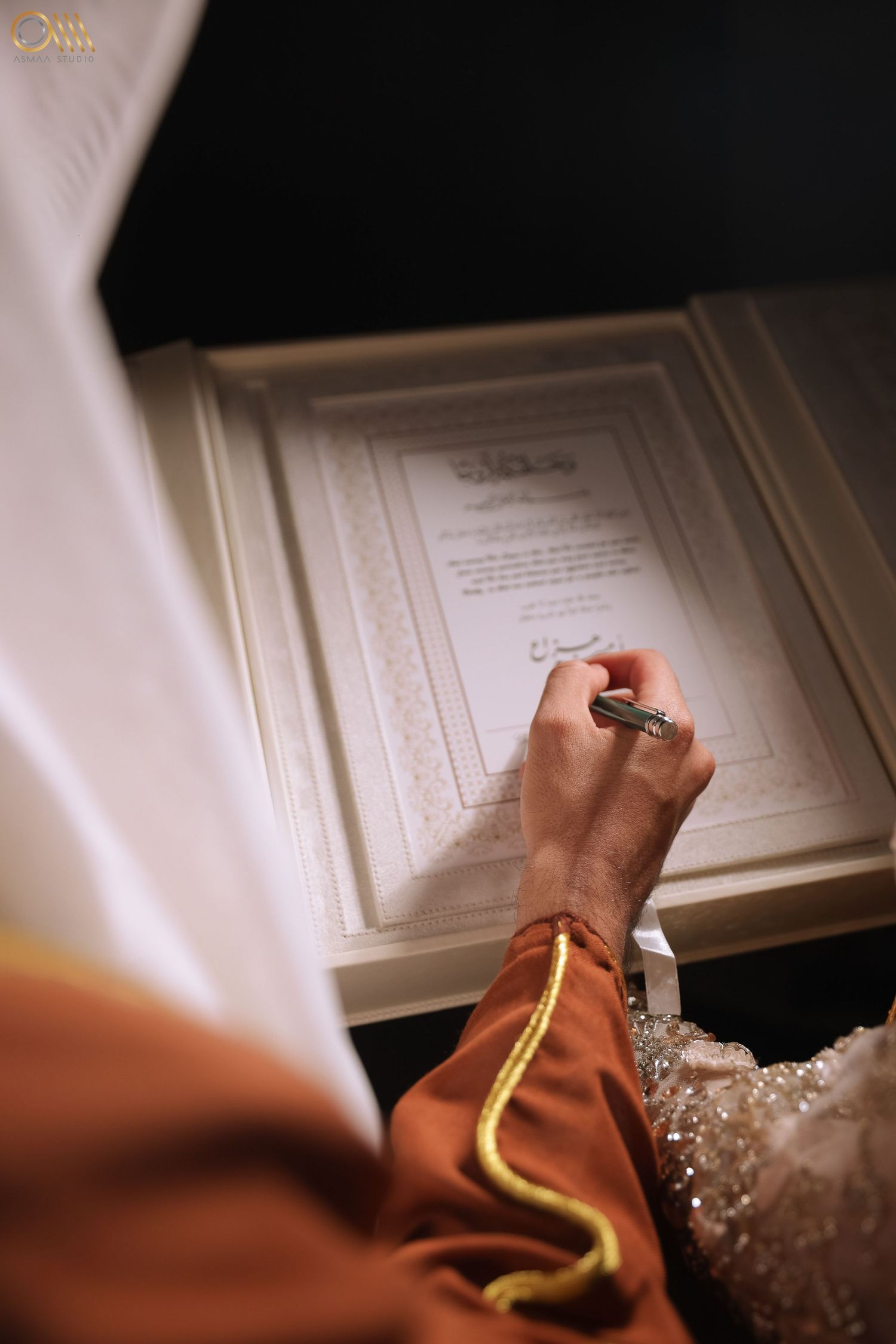 Hands signing a marriage contract document with ornate jewelry visible.