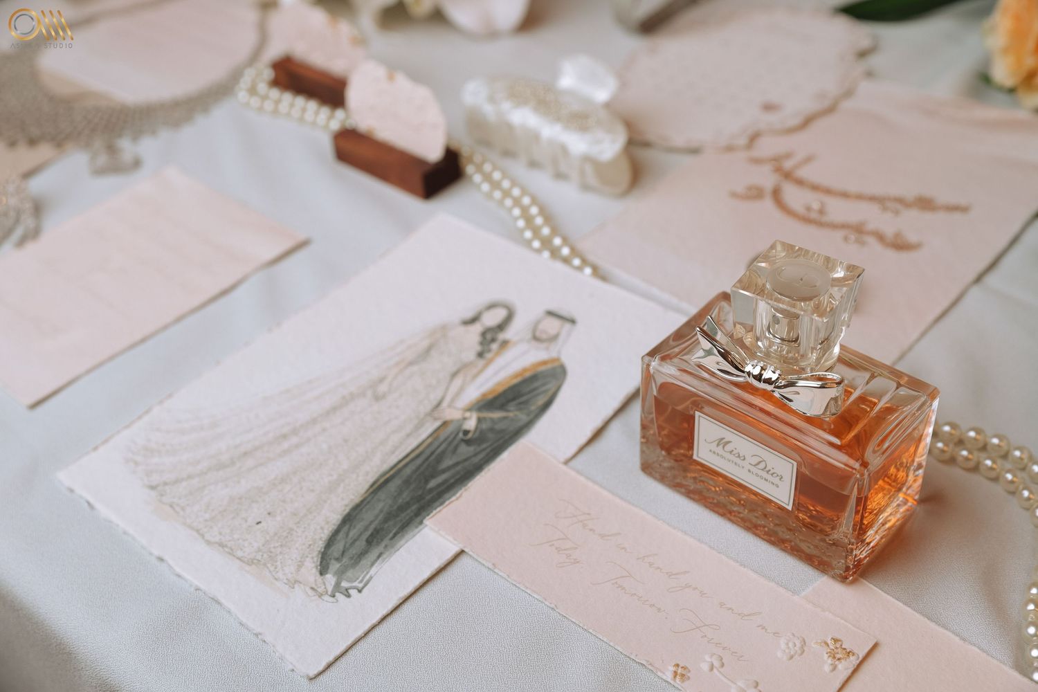 Wedding details flatlay with perfume bottle, jewelry, and delicate paper elements in soft lighting.