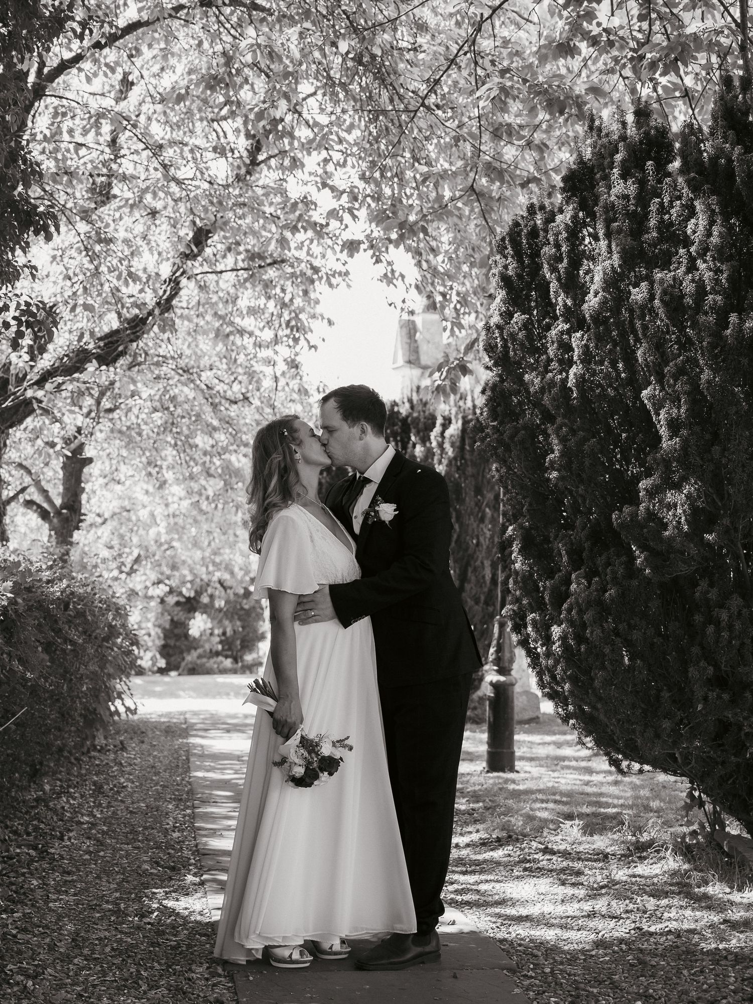 Bride and groom kissing along tree covered path