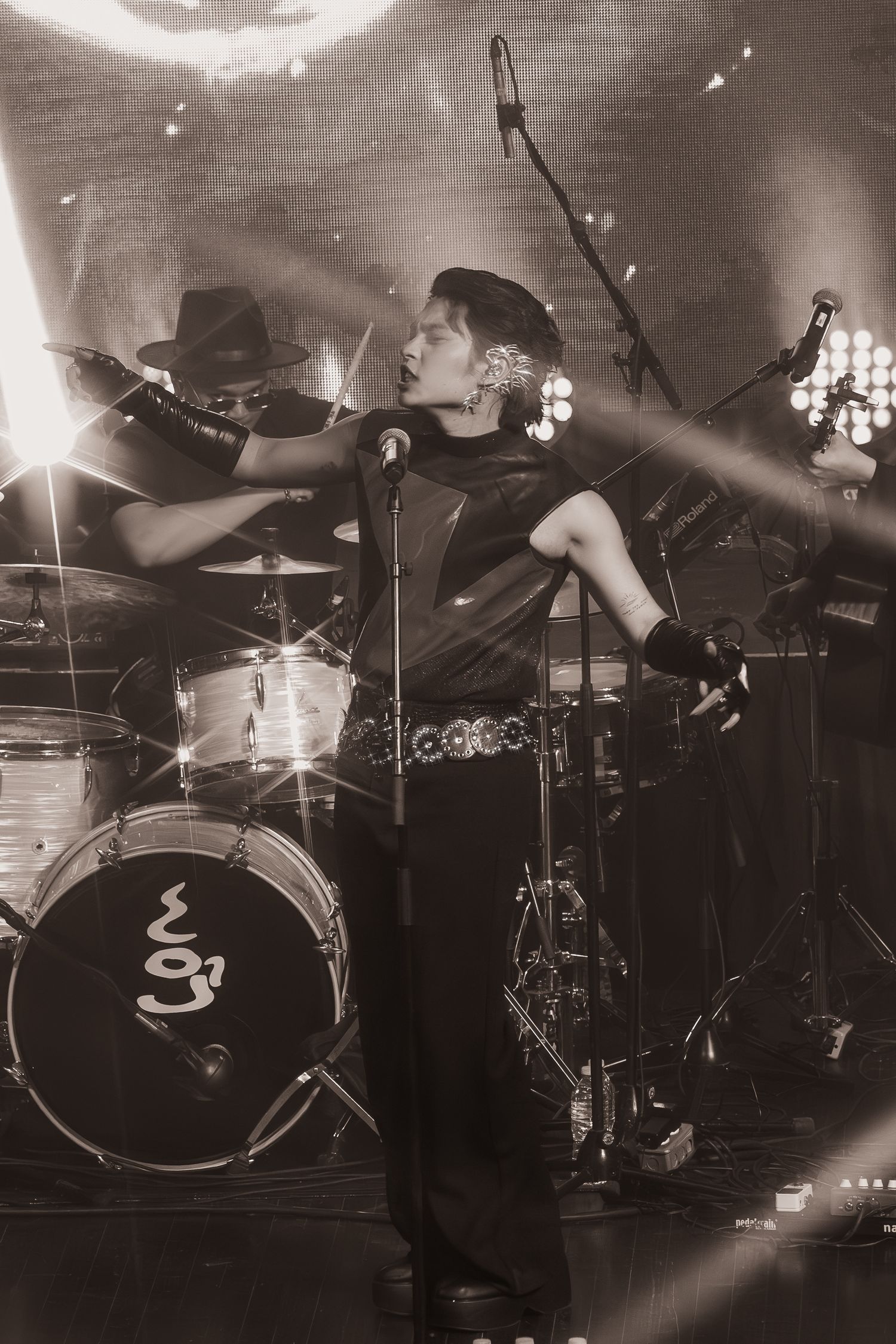 Black and white concert photo showing silhouettes of performers with dramatic stage lighting.