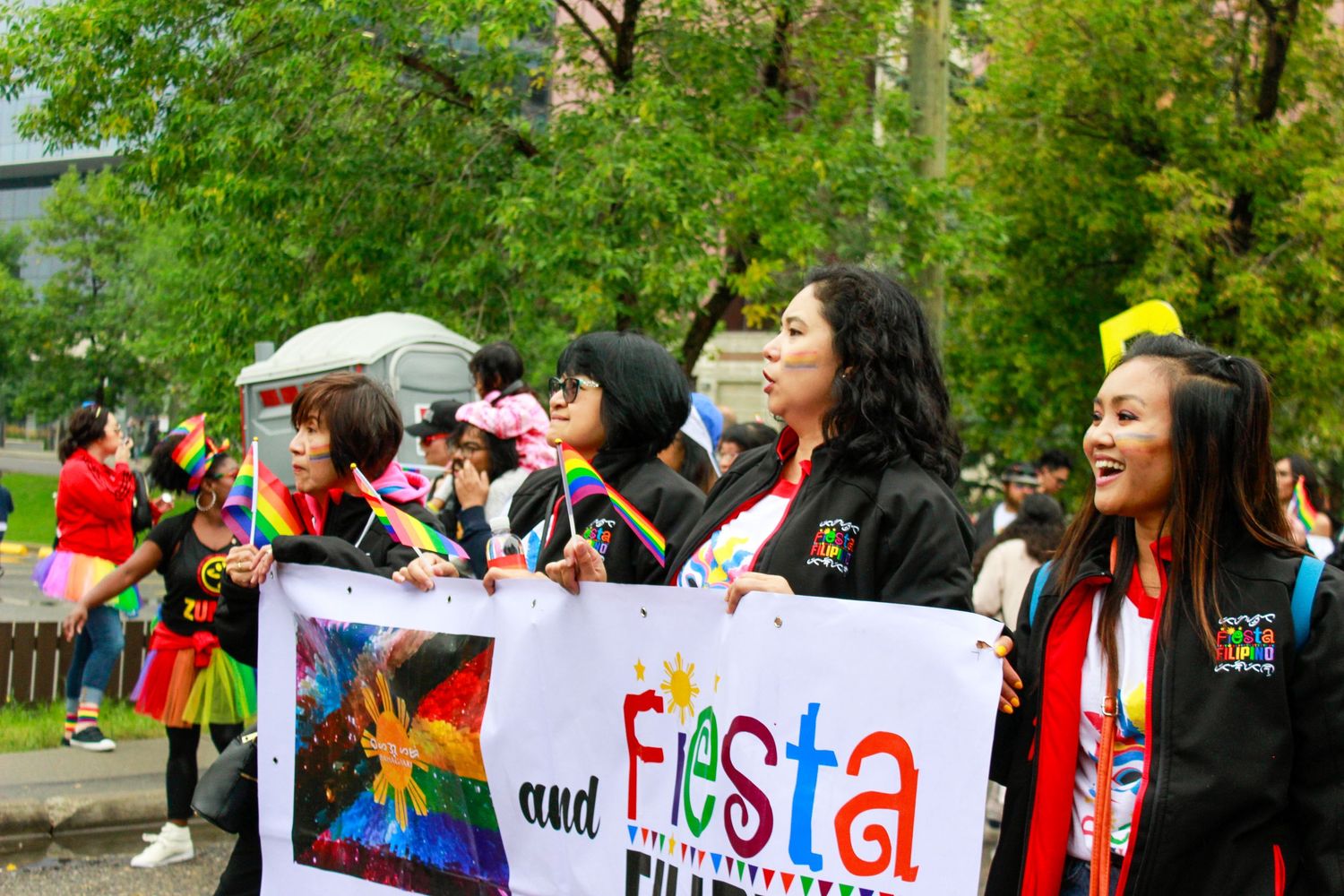 Crowd holding rainbow flags and signs at an outdoor pride celebration in a park setting.