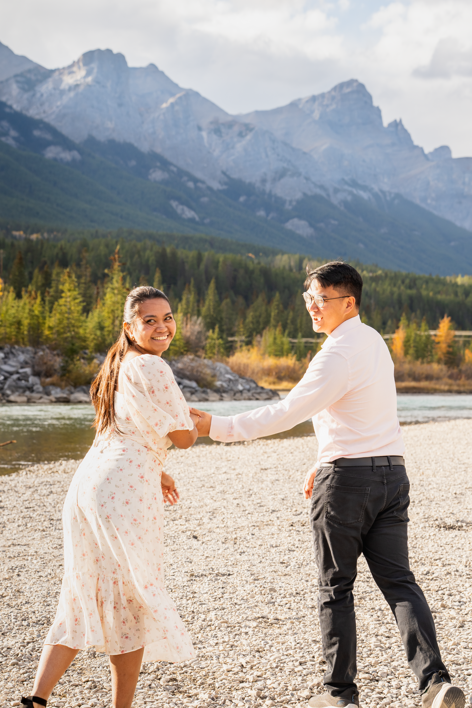 Couple dancing on rocky riverbank with mountain landscape in the background.