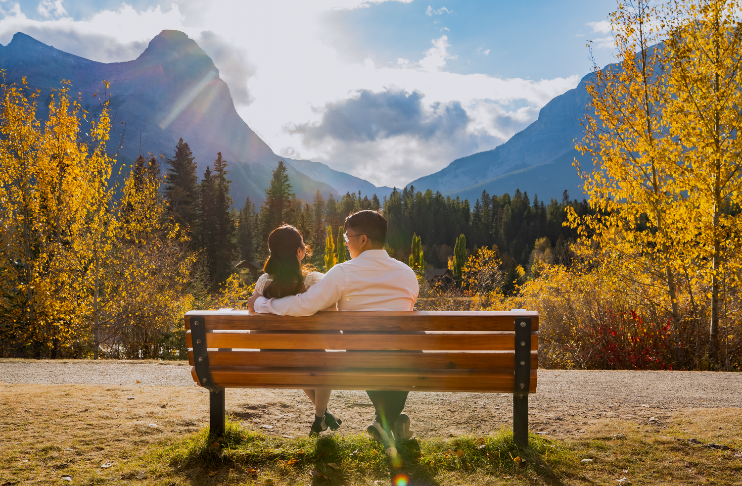 Panoramic mountain landscape with autumn trees and a bench overlooking snow-capped peaks.