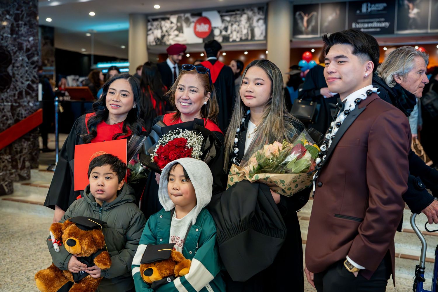 Family group photo at graduation ceremony with stuffed mascots and flowers.