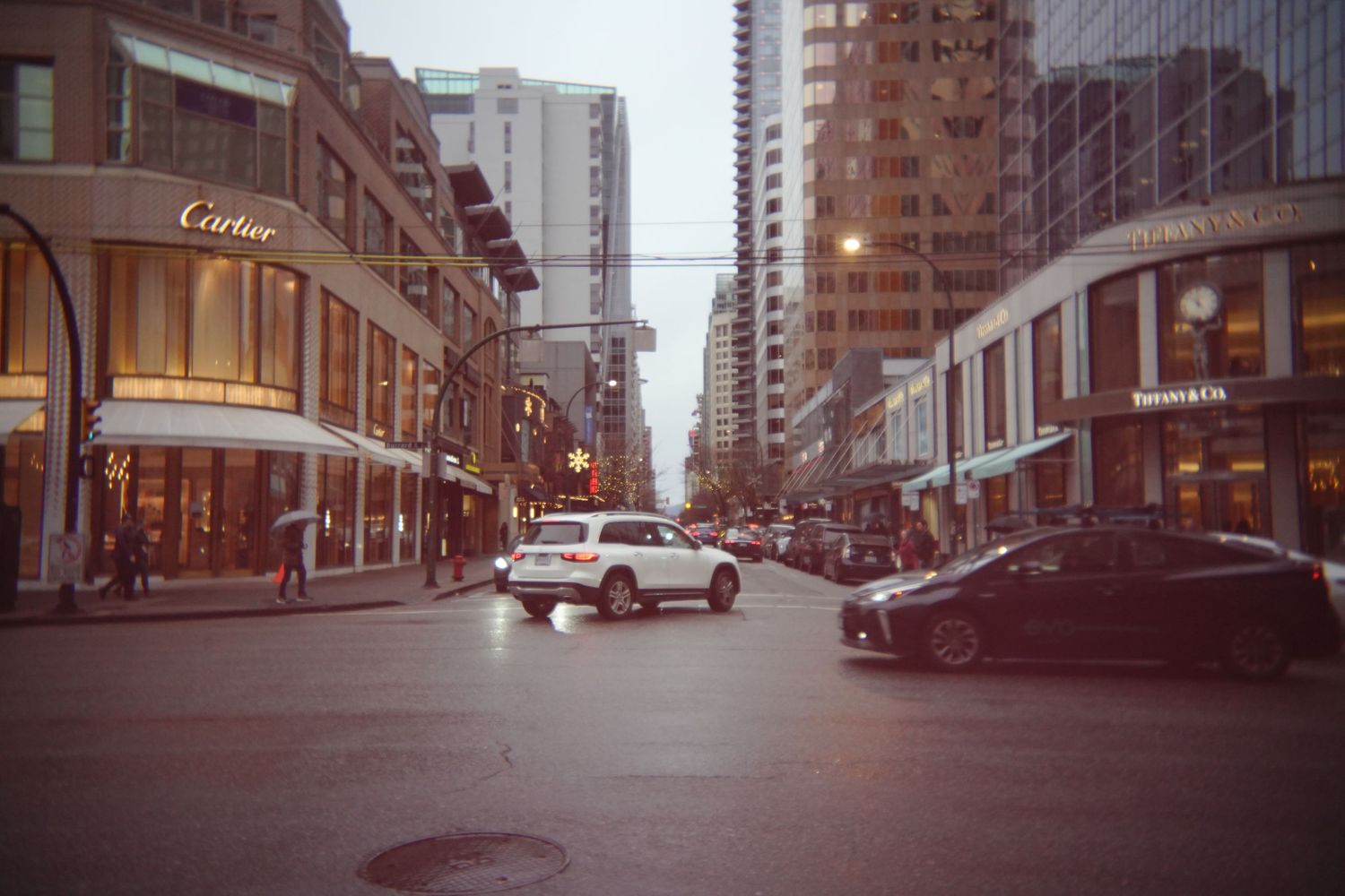 Downtown city street with modern buildings and light traffic on a cloudy day.
