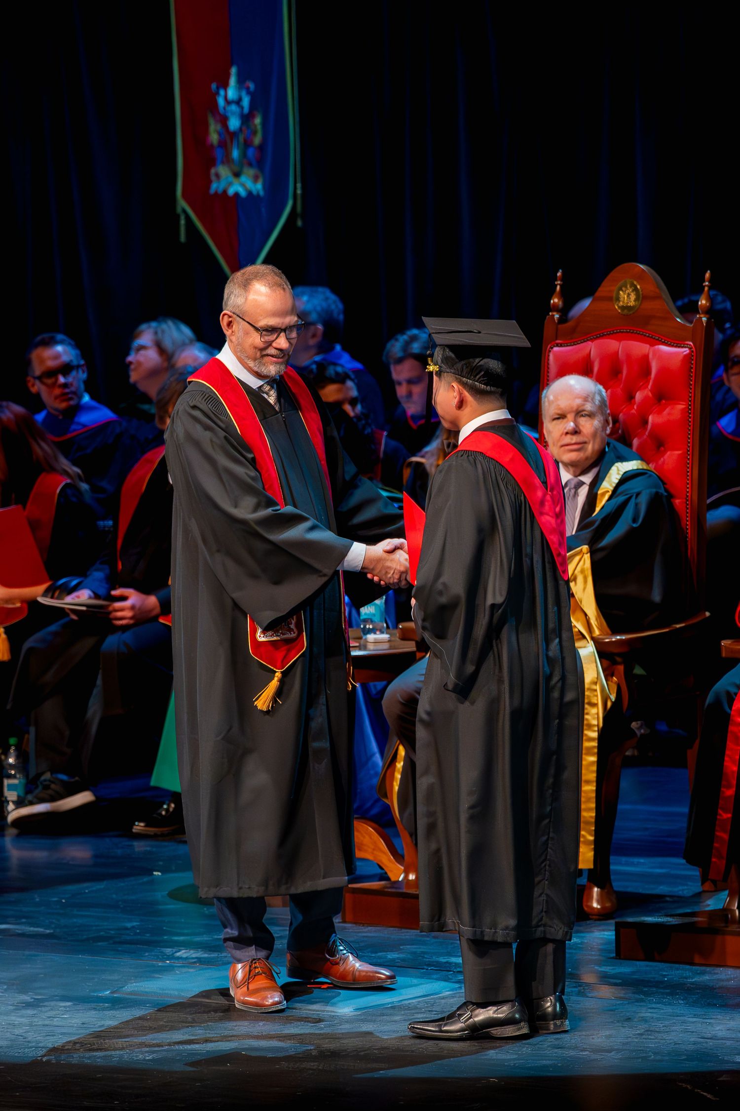 Academic graduation ceremony with robed faculty members on stage during a formal procession.