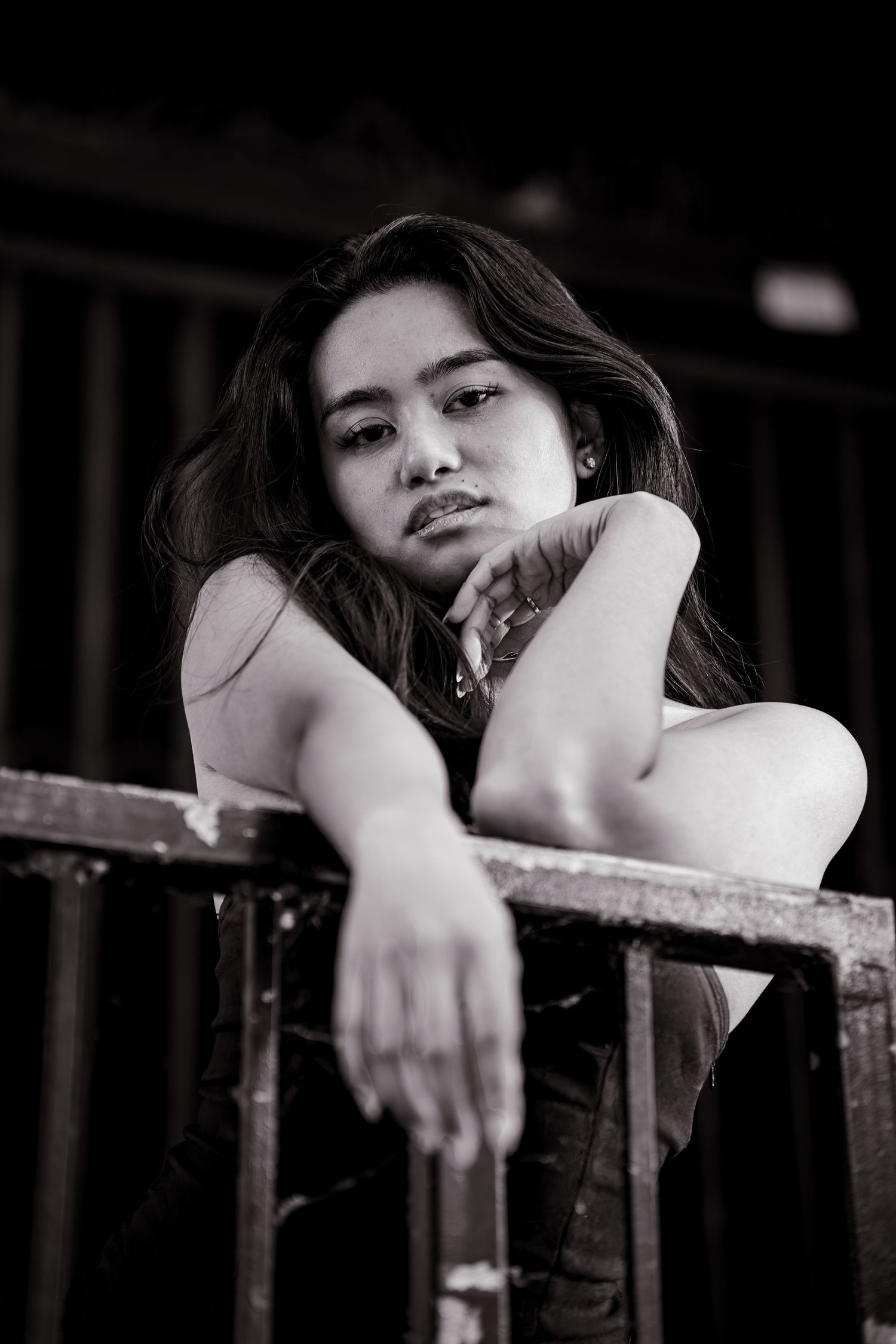 Black and white portrait of a model leaning on railing in moody lighting.