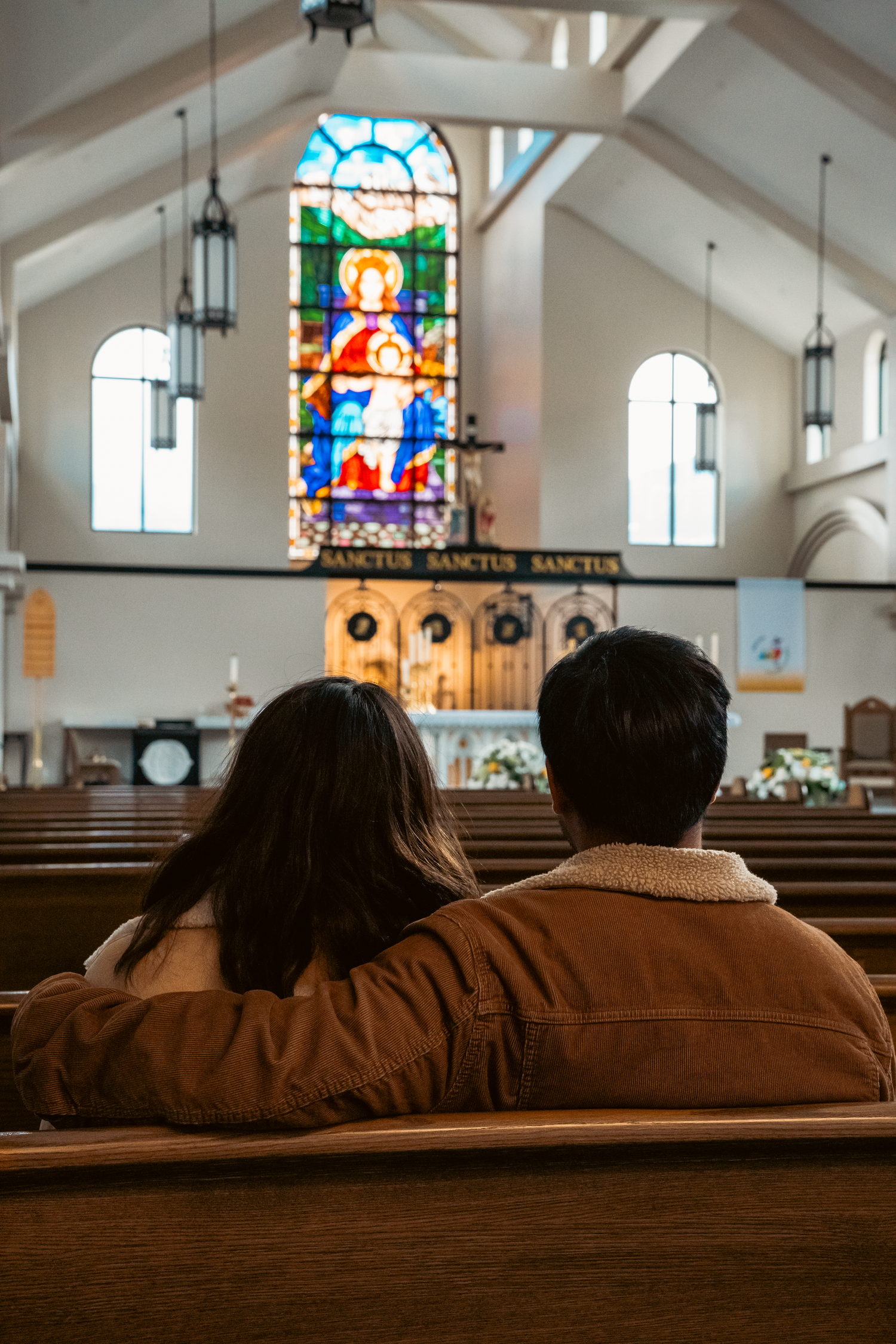 Interior of a church with stained glass windows and wooden pews in soft lighting.