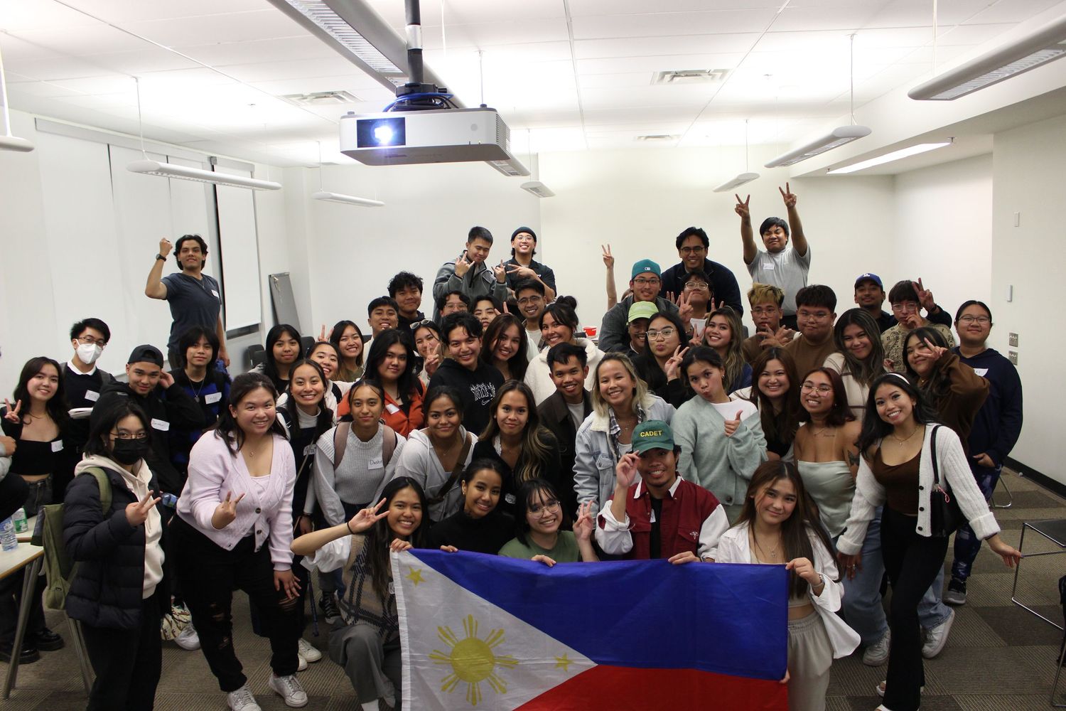 Large group photo of students posing with Philippine flag in classroom setting.