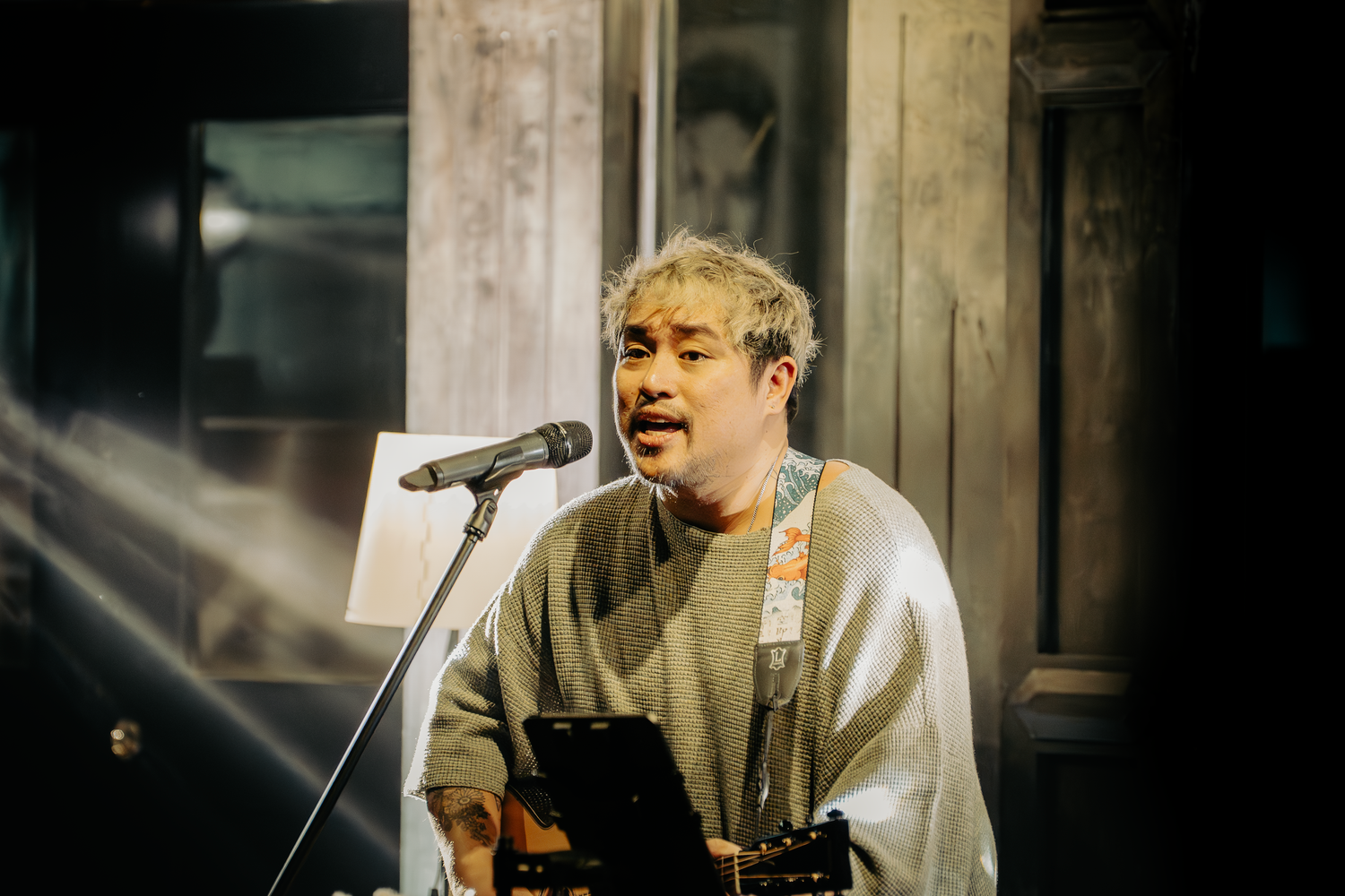 Musician performing with acoustic guitar under dramatic stage lighting.